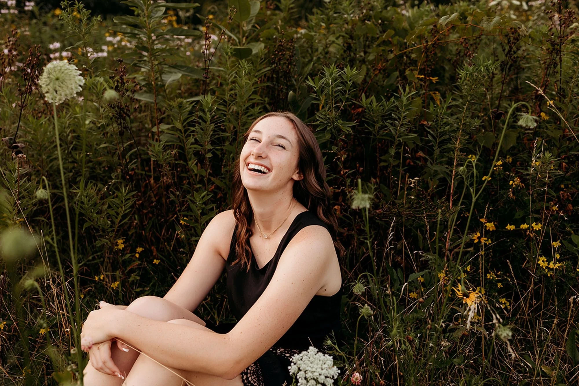 Sheridan High School senior photos featuring a smiling senior surrounded by wildflowers, capturing her relaxed personality and natural joy in a beautiful outdoor setting.