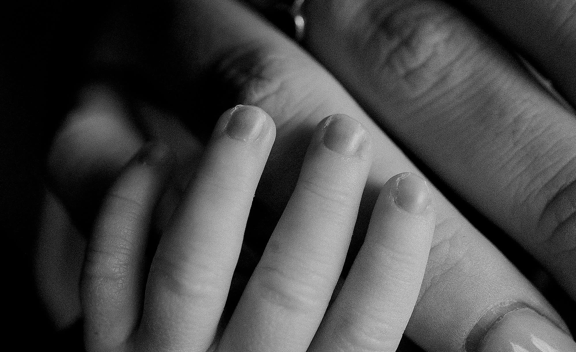 Close-up black and white photo of fingers touching a reflective surface, possibly a mirror, with a focus on the fingertips.