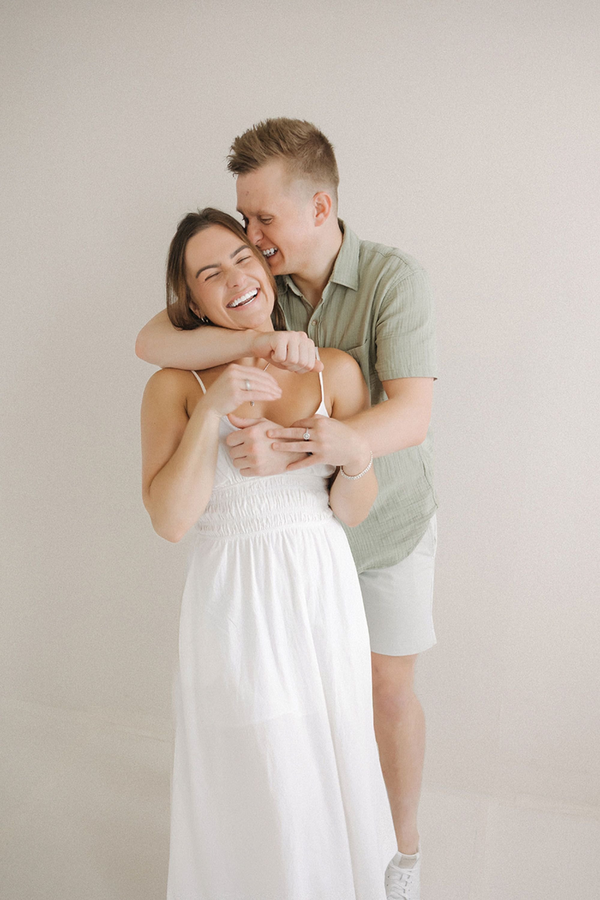 A beautiful couple shares a playful embrace in a bright, minimalist studio, capturing genuine laughter during a Studio Family Photos session at Studio Loft 18.