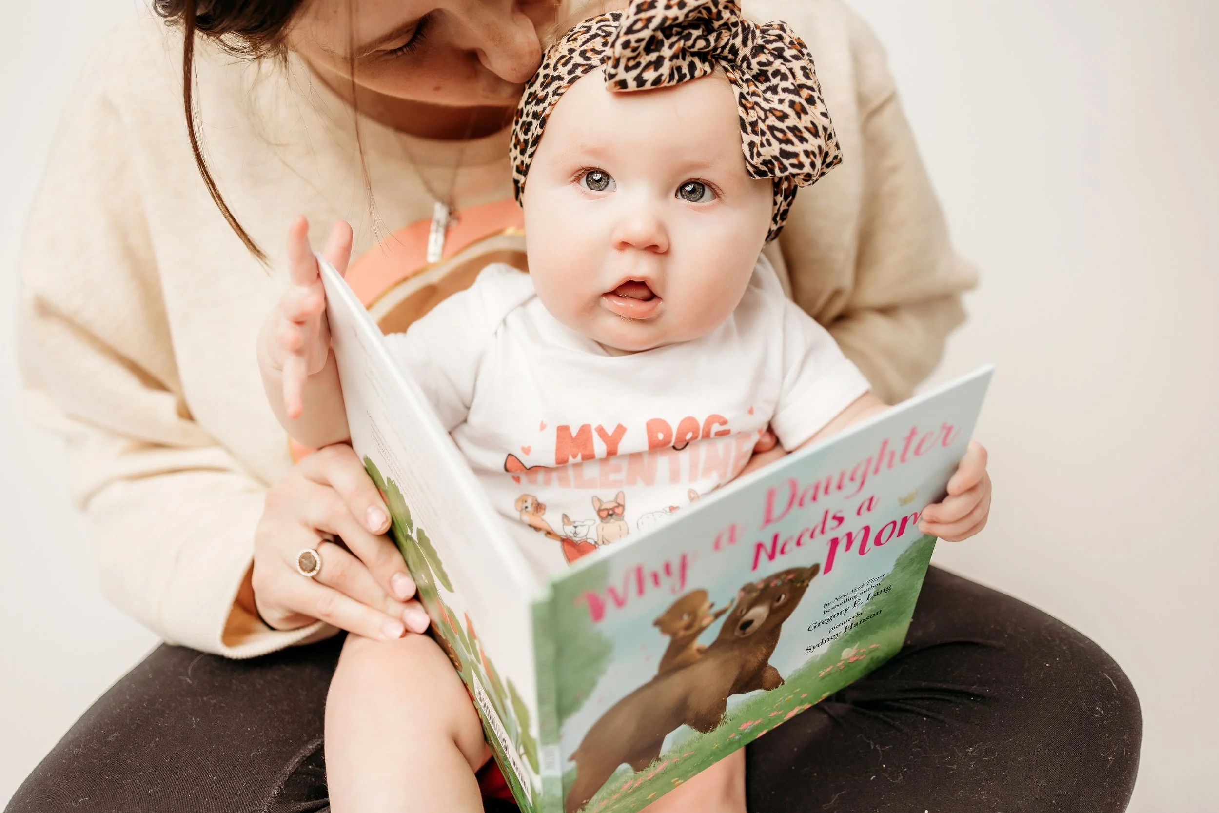 A woman holds her baby and reads, creating a heartwarming image for 6-month milestone photo ideas.