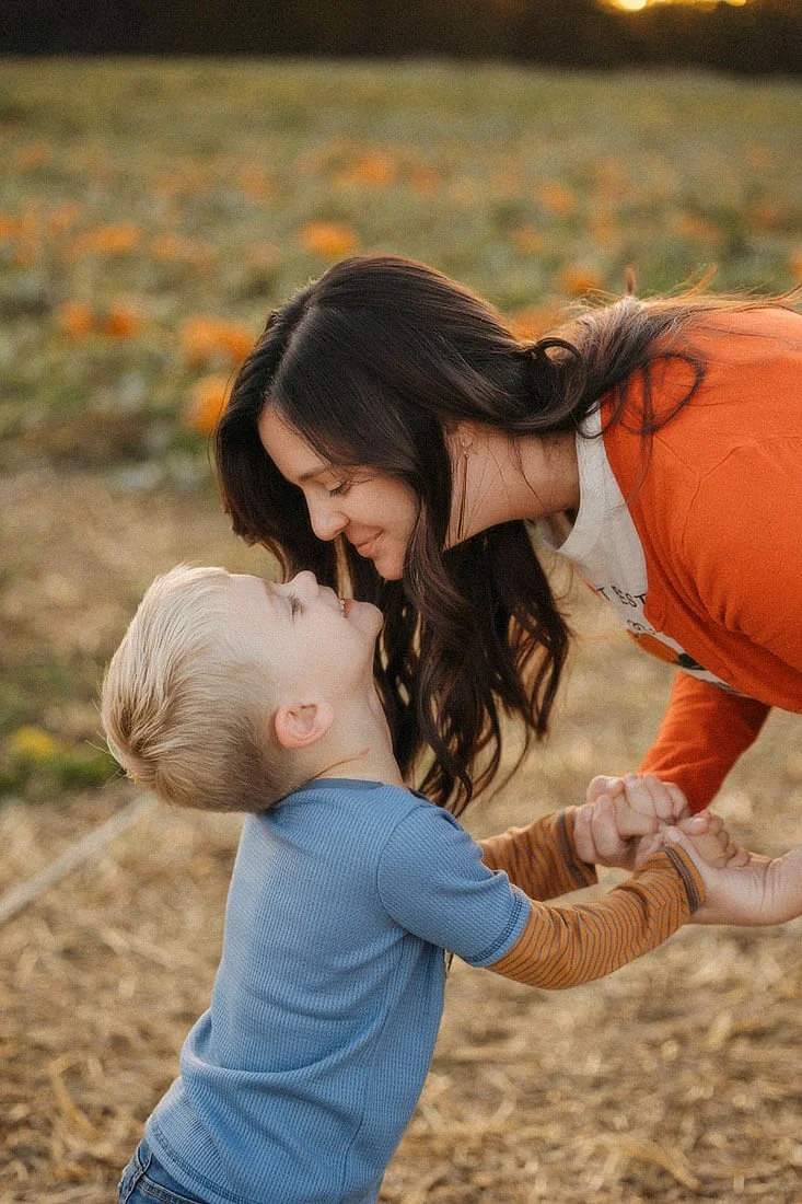 Mother playfully leaning toward her smiling young son in the pumpkin patch during a warm autumn family session at Dull’s Pumpkin Harvest