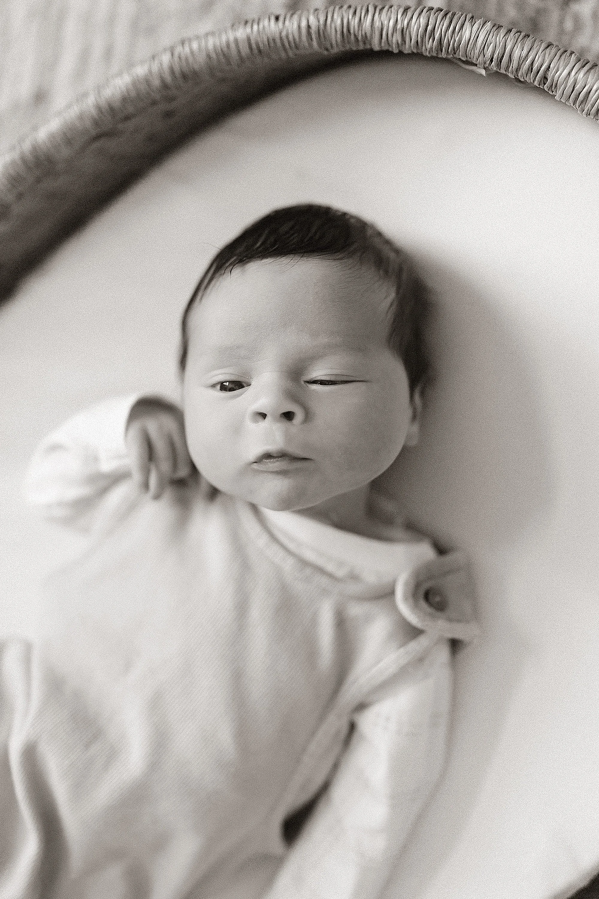 Black and white photo of a newborn baby lying on a white surface, wearing a light-colored outfit with buttons.