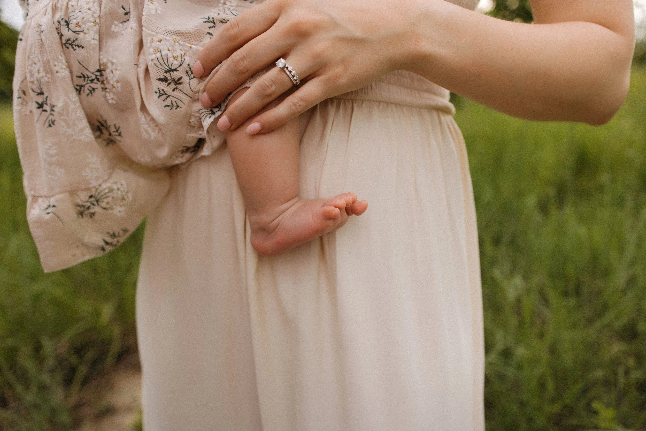 A mother holds her infant in a vibrant field, symbolizing love and connection in a serene outdoor setting