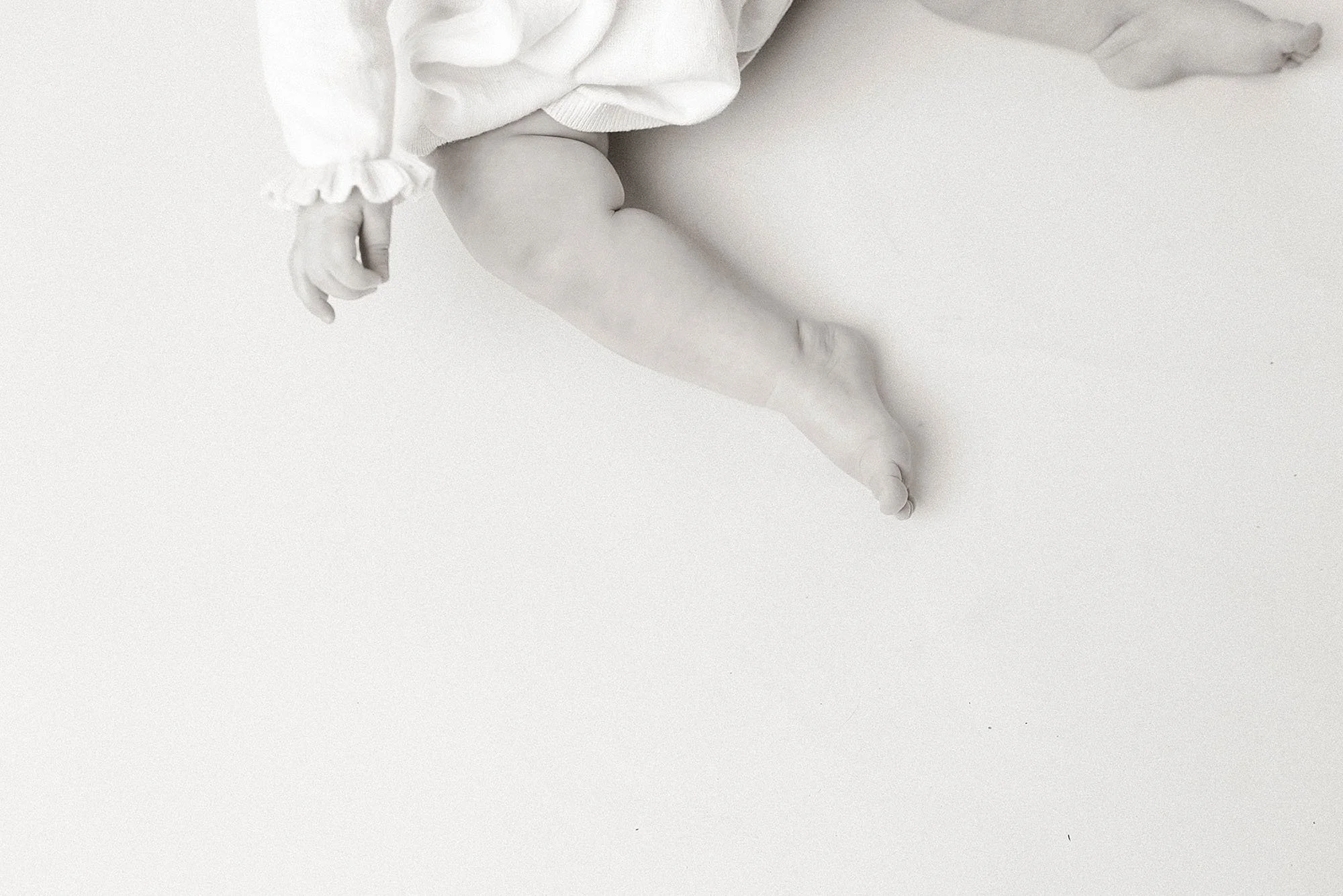 A baby on its back in a white room, marking their first birthday milestone in a photography session in Westfield, Indiana