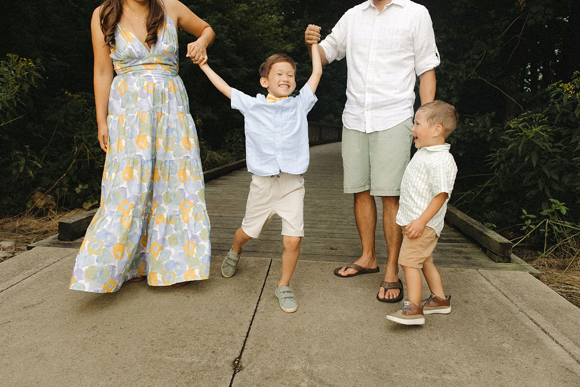 Parents swinging their laughing son between them on a boardwalk, younger brother joining in, during a Flat Fork Creek Park family photo session