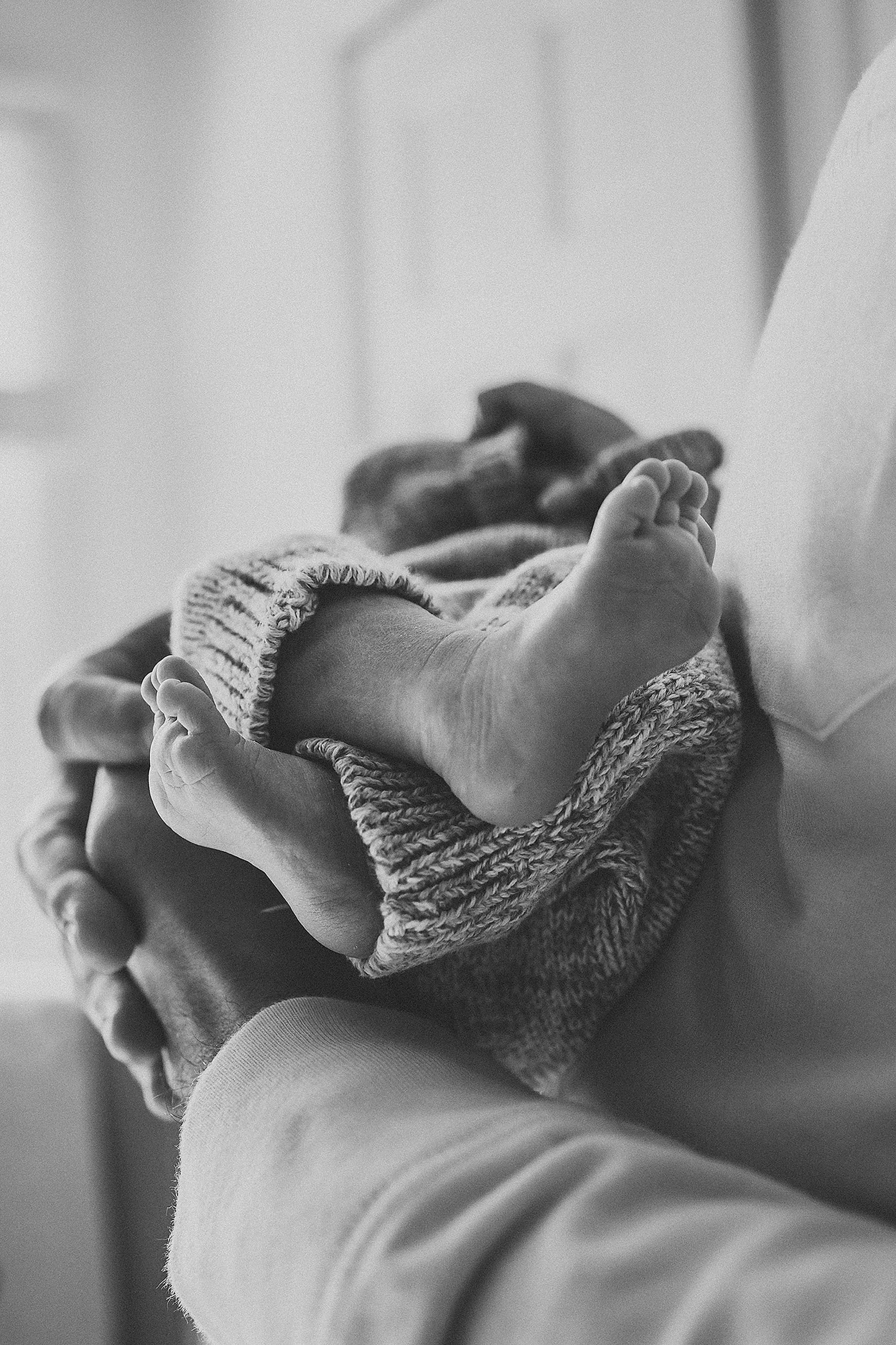 A newborn baby lying on a person's arm, wrapped in a knitted blanket.