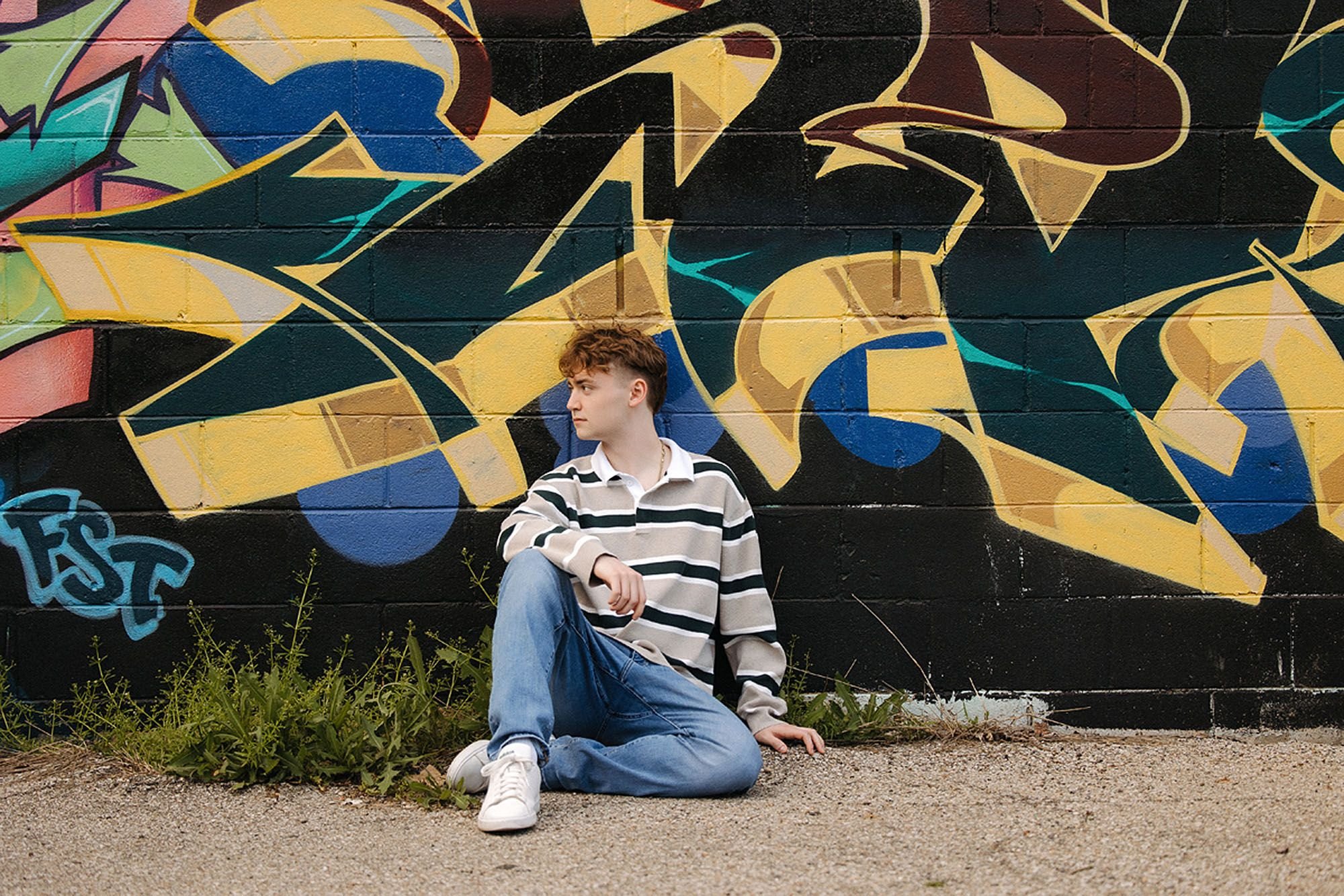 High school senior sitting in front of a colorful graffiti mural during a modern urban senior photo session in Indianapolis
