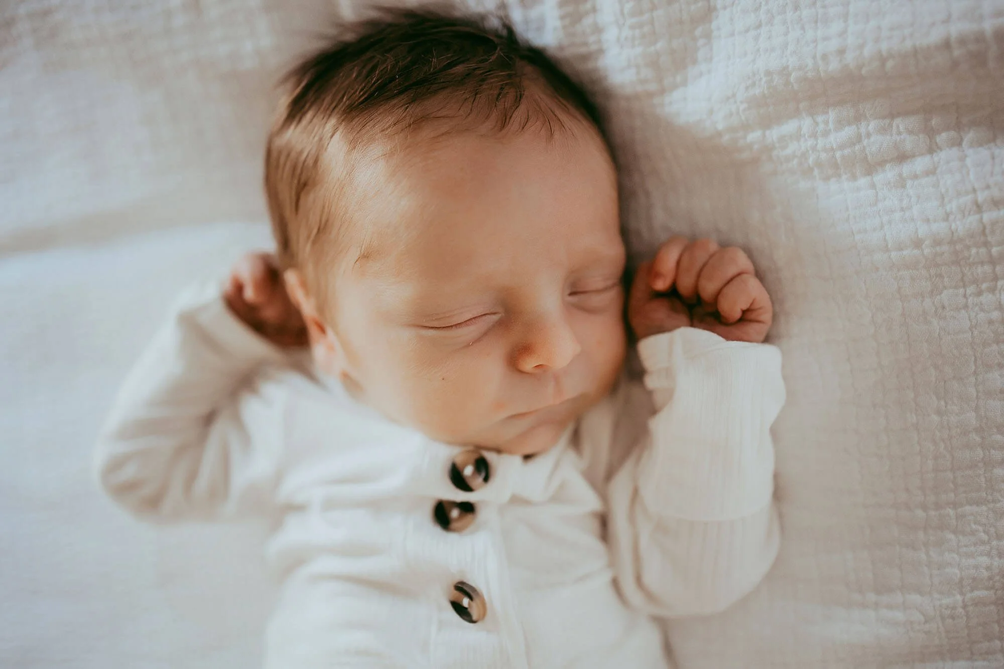 A sleeping baby on a white blanket, beautifully photographed in a New Baby Photos session