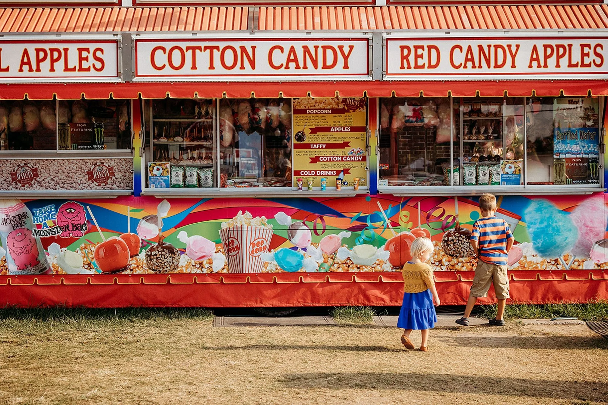 Children stand happily in front of a bright cotton candy stand during a carnival a carnival photo session in Indiana