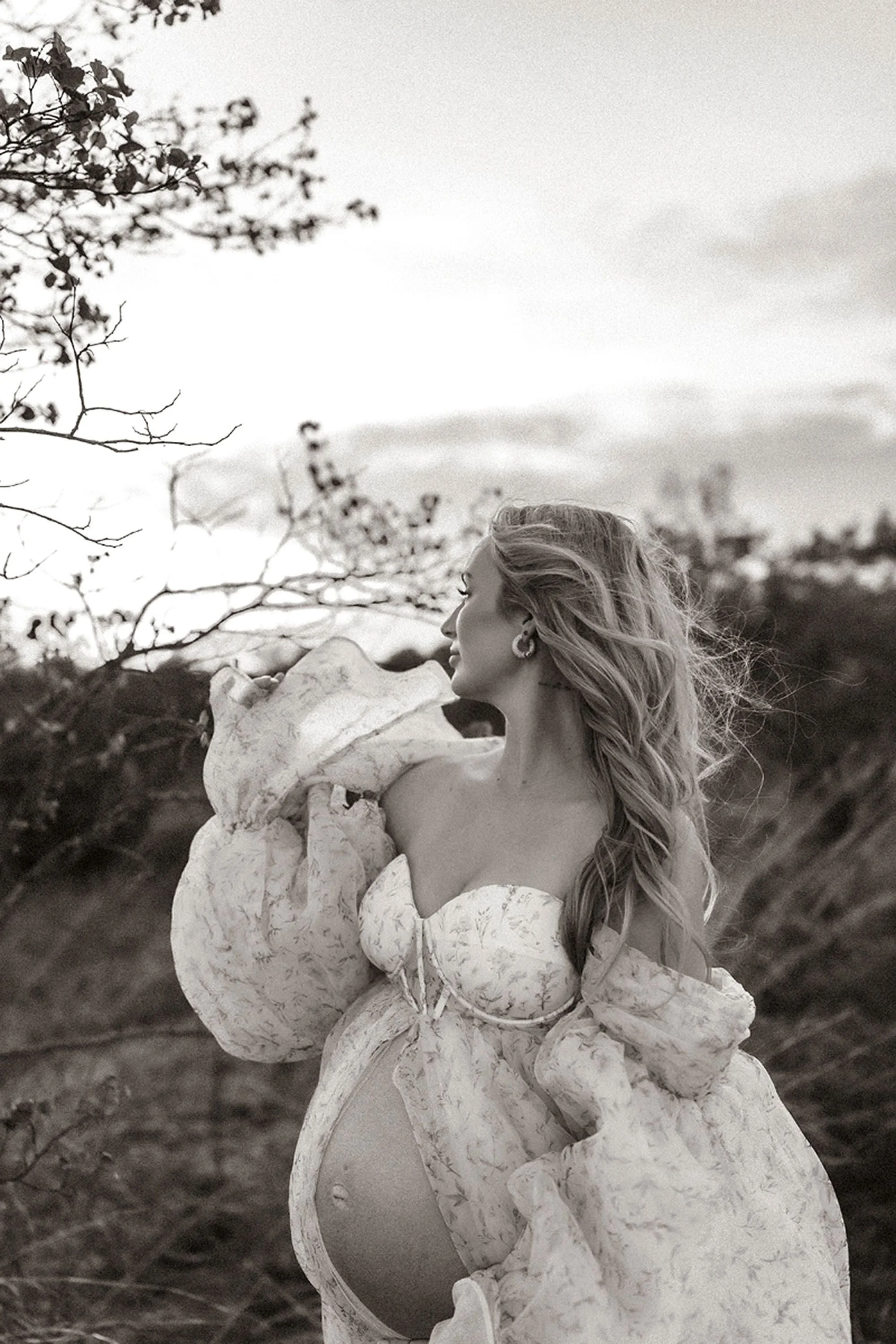 Black and white maternity photos in Central Indiana close-up of a pregnant woman in profile with windswept hair, hand resting near her shoulder against a dusky sky