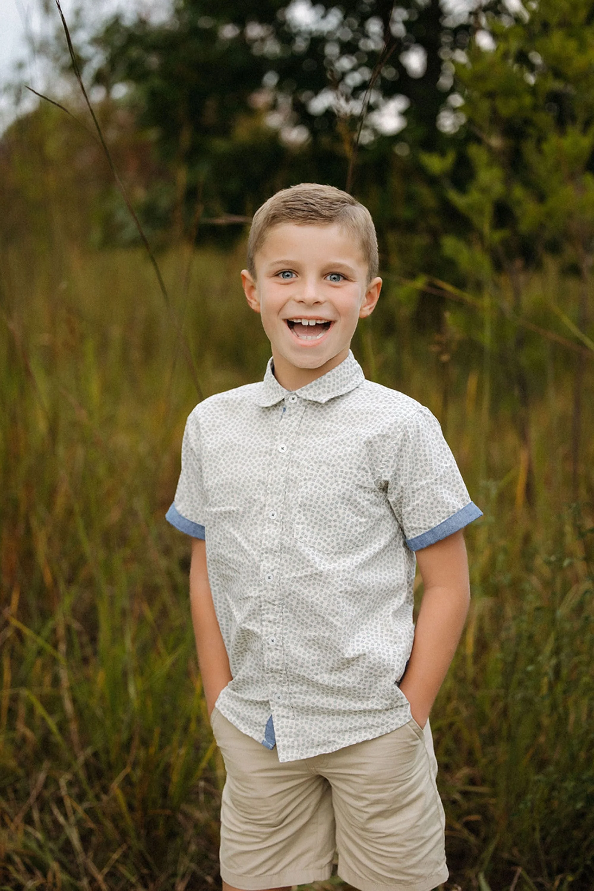 Smiling young boy standing in a grassy field during summer family photos at Carmel, Indiana with a natural outdoor backdrop