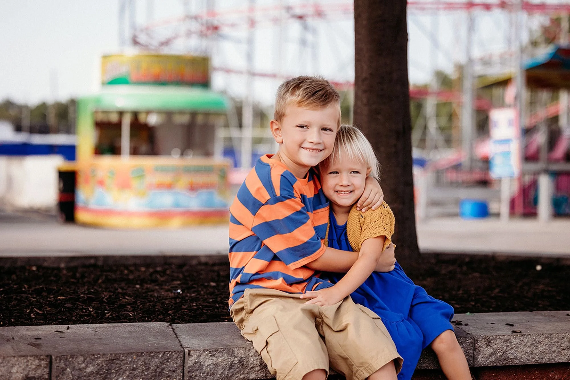 Children pose happily on a bench with a brightly lit ferris wheel in the background at an Indiana carnival photo session