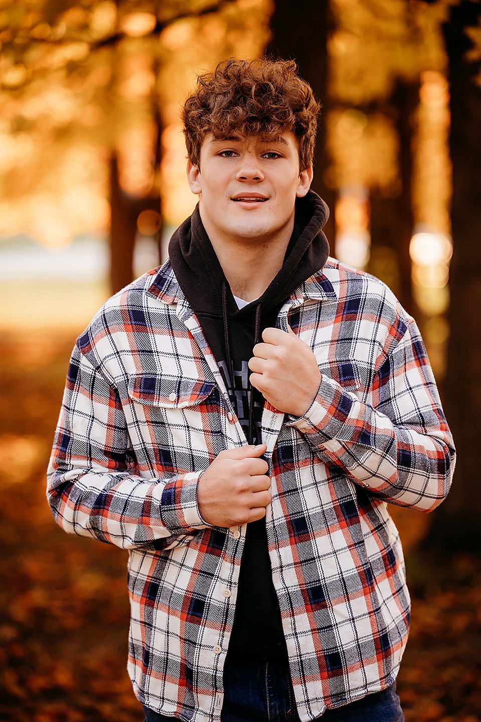 Senior pictures in Indianapolis with teen boy in plaid shirt smiling in fall trees