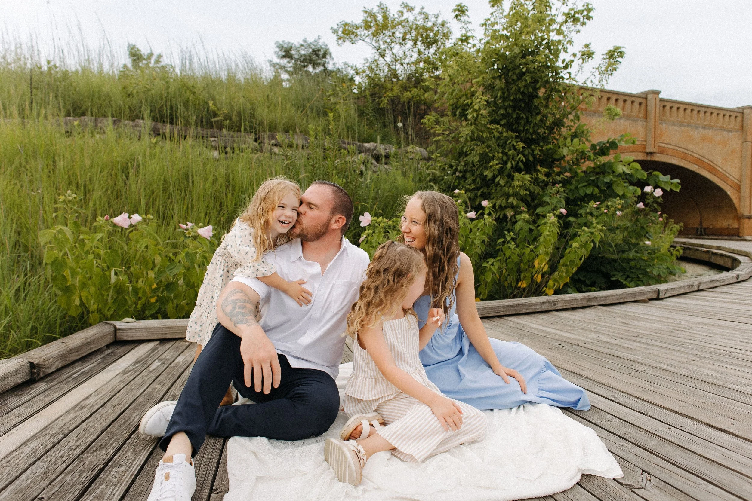 An extended family poses on a wooden boardwalk, with a bridge in the background, capturing a moment together