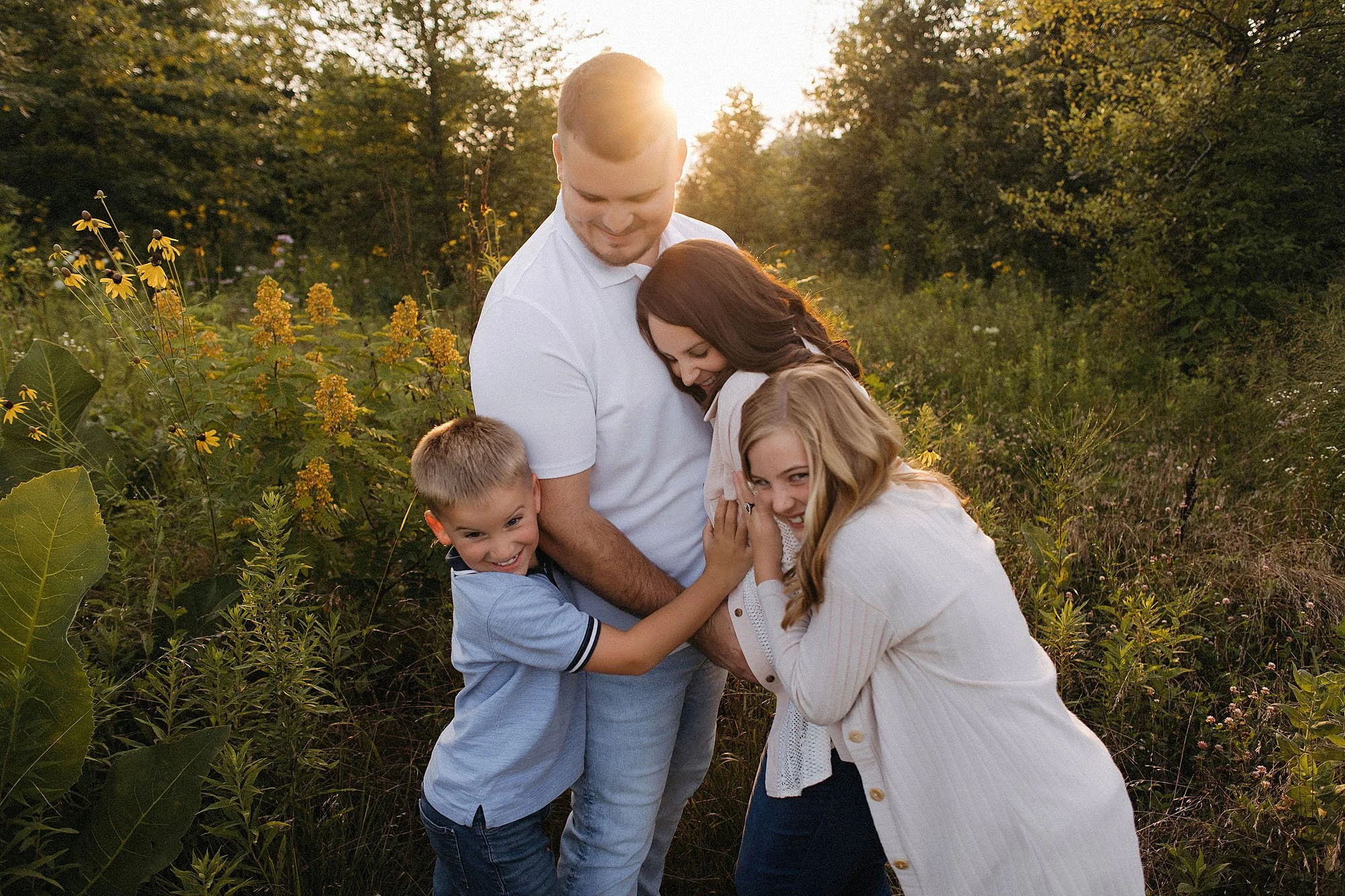 Expecting parents with their two children sharing a candid moment in a wildflower field at golden hour