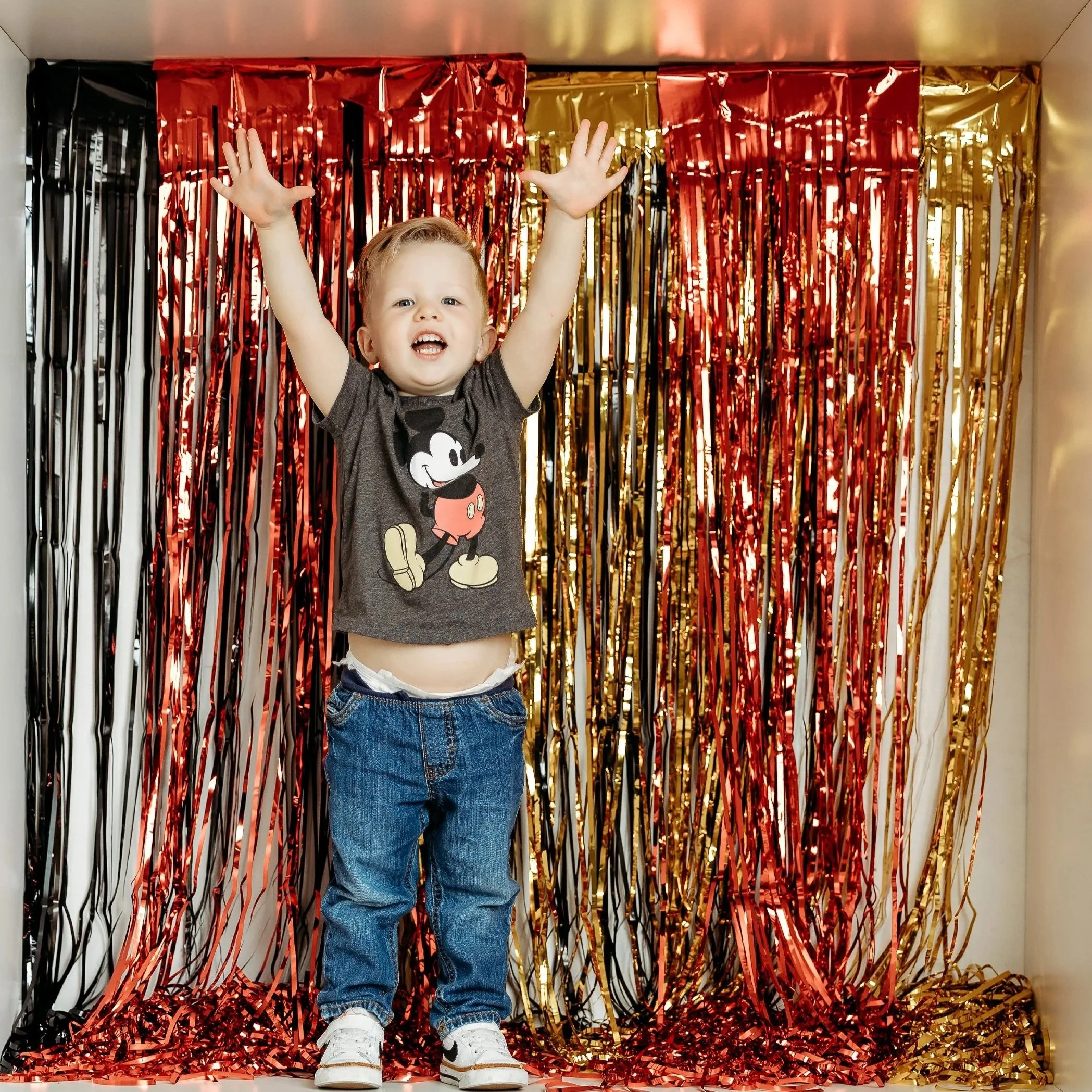 Happy toddler celebrating Two-dles and two-year milestone photos with playful arms raised and a festive birthday backdrop