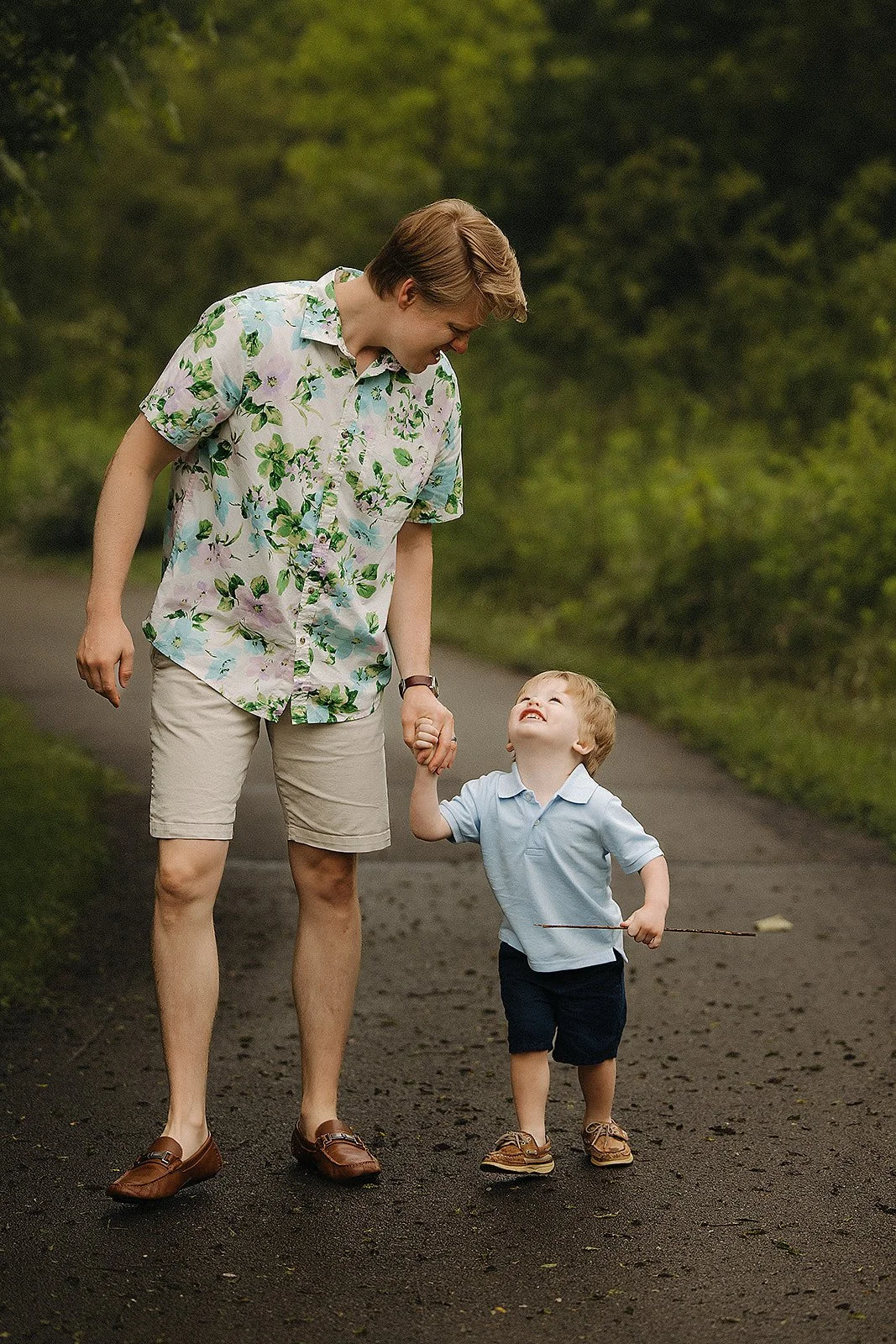Father holding hands with his young son while walking on a wooded path in Indianapolis.