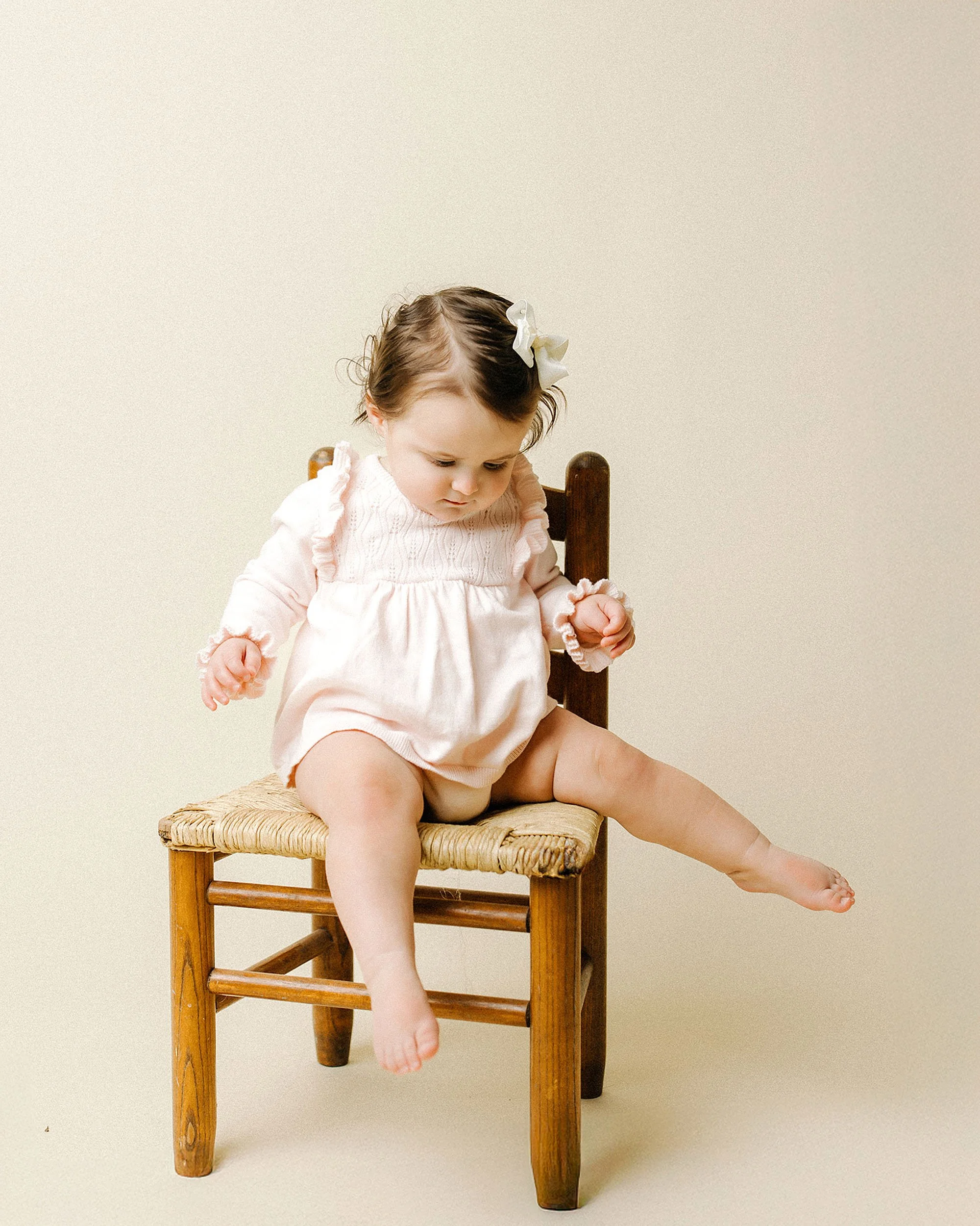A baby sits on a wooden chair, celebrating their first birthday milestone in Westfield, Indiana