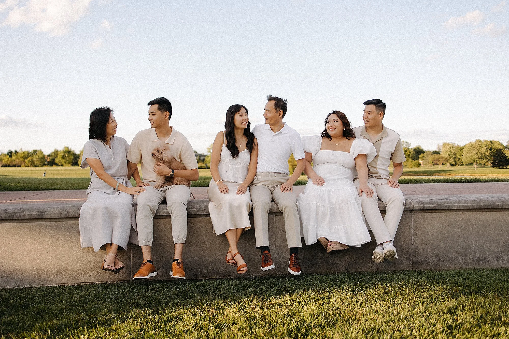 Multi-generational family in coordinated neutral outfits sitting together outdoors during golden hour, showcasing elegant color coordination and timeless style