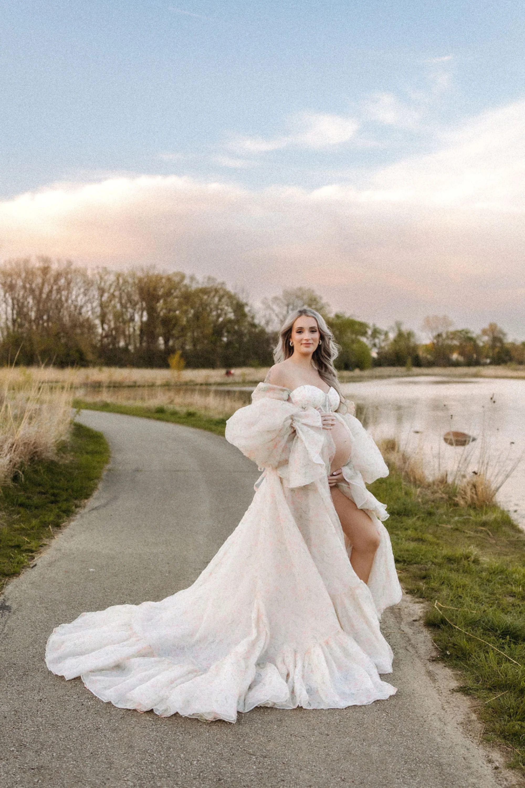 Romantic maternity portrait of a mom-to-be in a flowing gown surrounded by warm sunset light and natural scenery.
