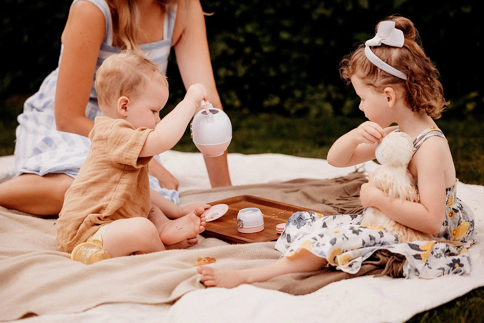 A woman and two children sit on a blanket in the grass during a backyard photography session in Indiana