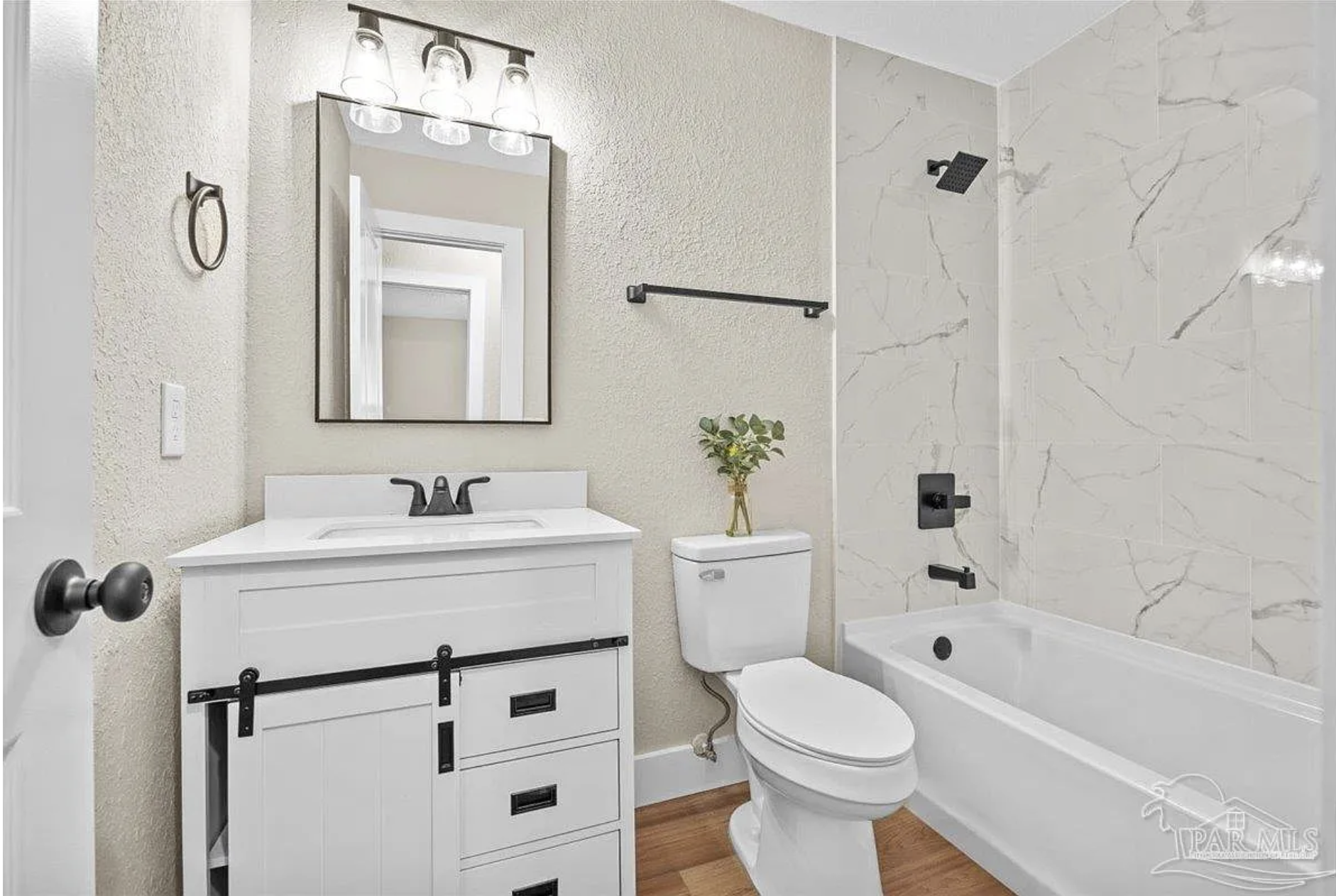 A modern bathroom with a white vanity, a mirror, a toilet, and a bathtub with a marble wall.