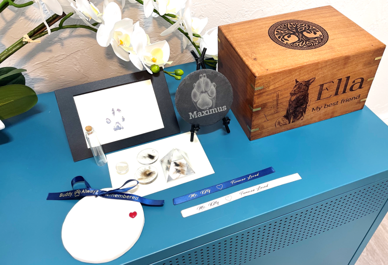 A vast array of urns are shown on a teal cabinet. They come in different material, such as wood, ceramic, or glass. The wood urns have pictures of the pet laser engraved onto the surface along with their name.