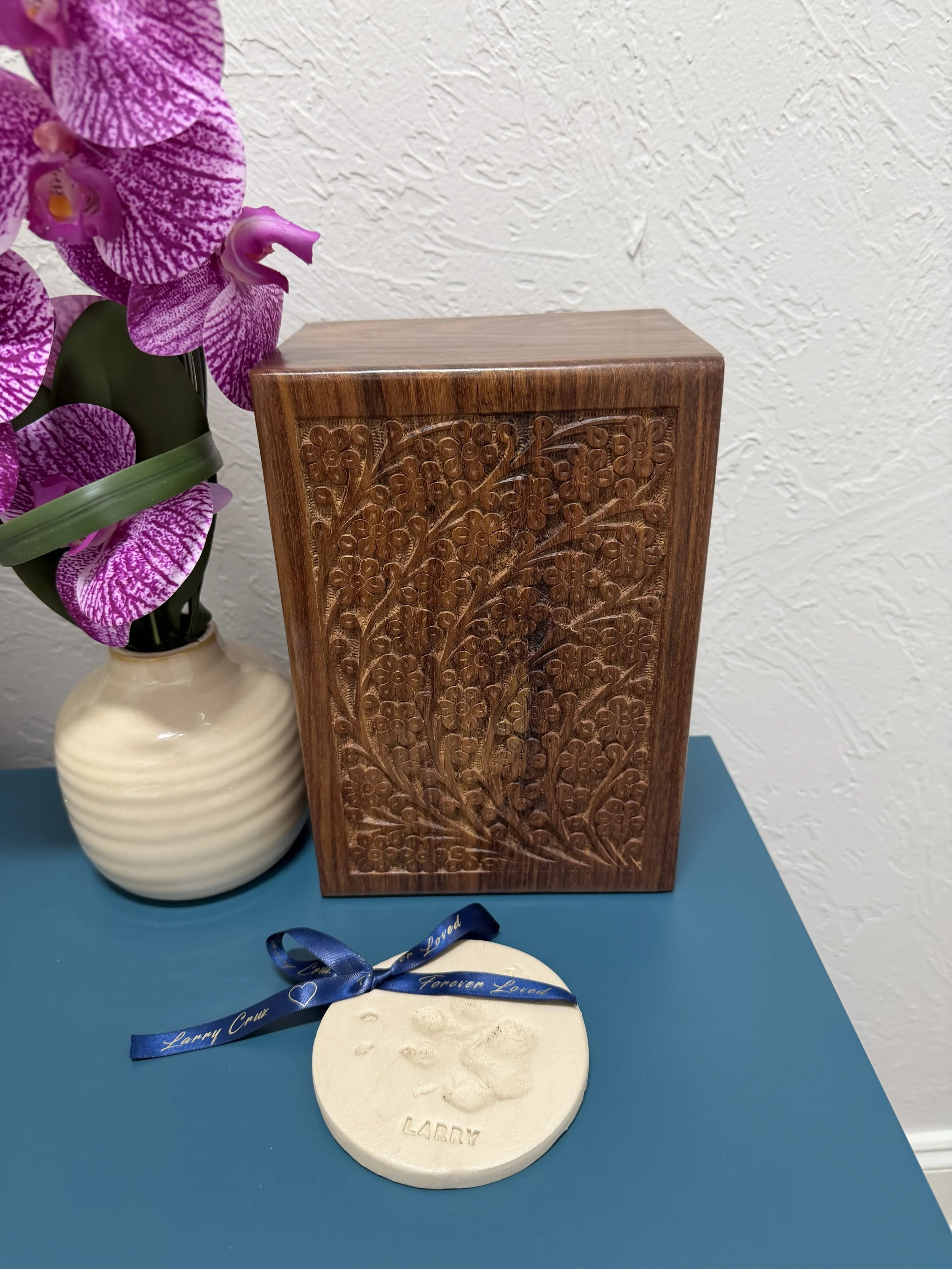 Engraved leaves on a wooden urn with a white clay paw print and custom ribbon