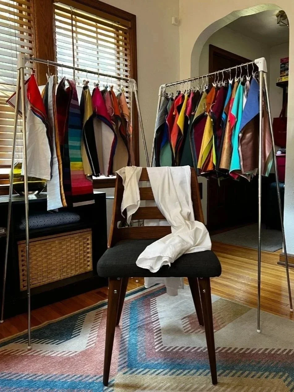 Setting for in-home color analysis.  Racks holding fabrics for each season and subseason in background with a chair front-center with white cap draped over it