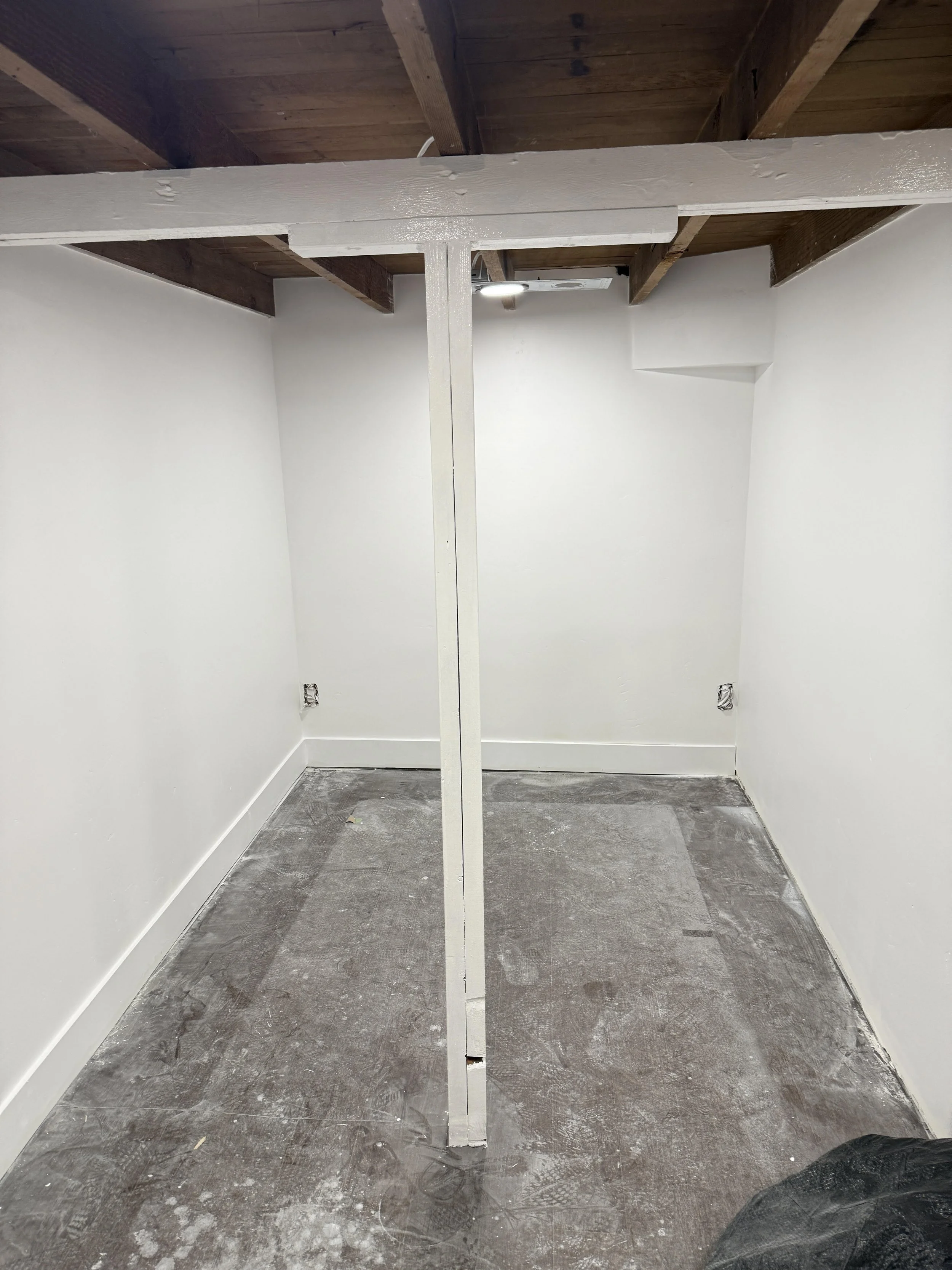 Empty small room under construction with drywall walls, a ceiling fan, and a partially painted wooden beam in the ceiling.