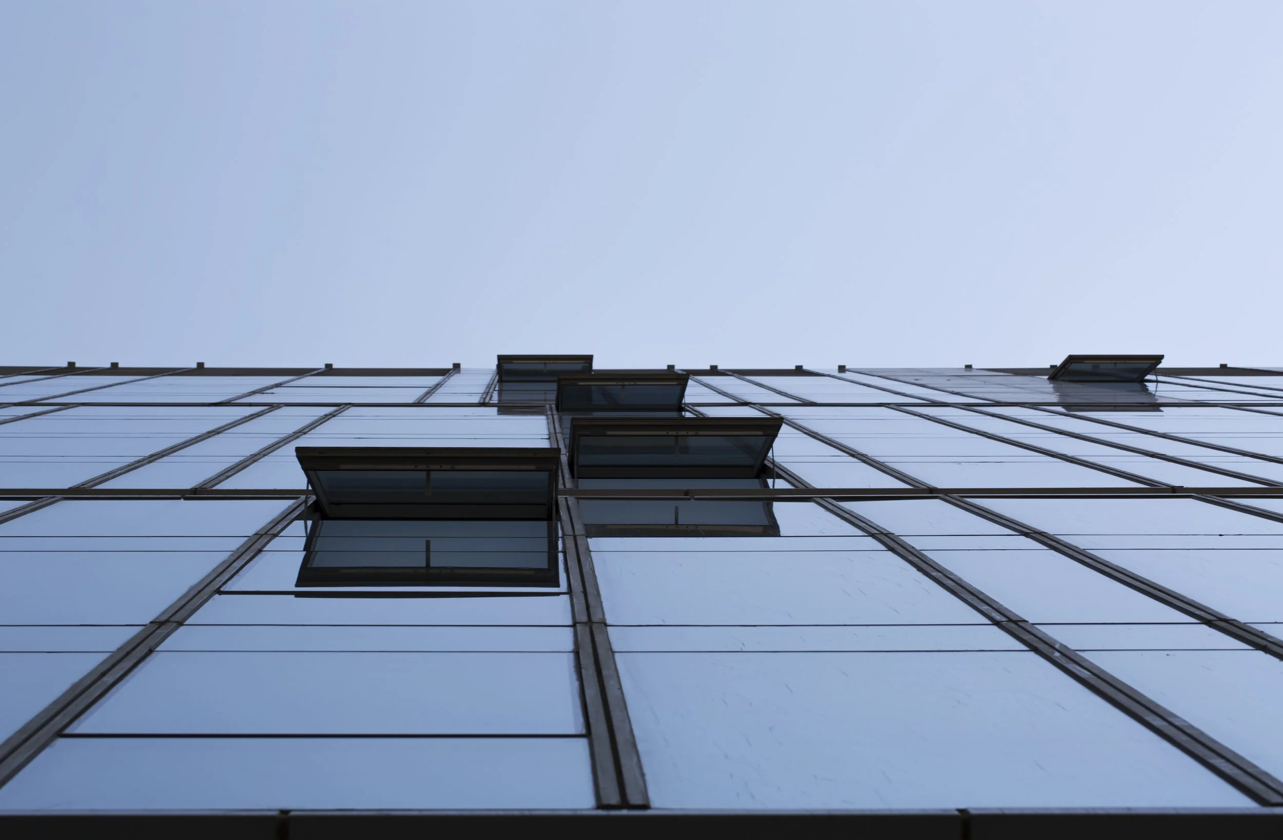 Low-angle view of a modern glass building with multiple open windows against a clear blue sky.