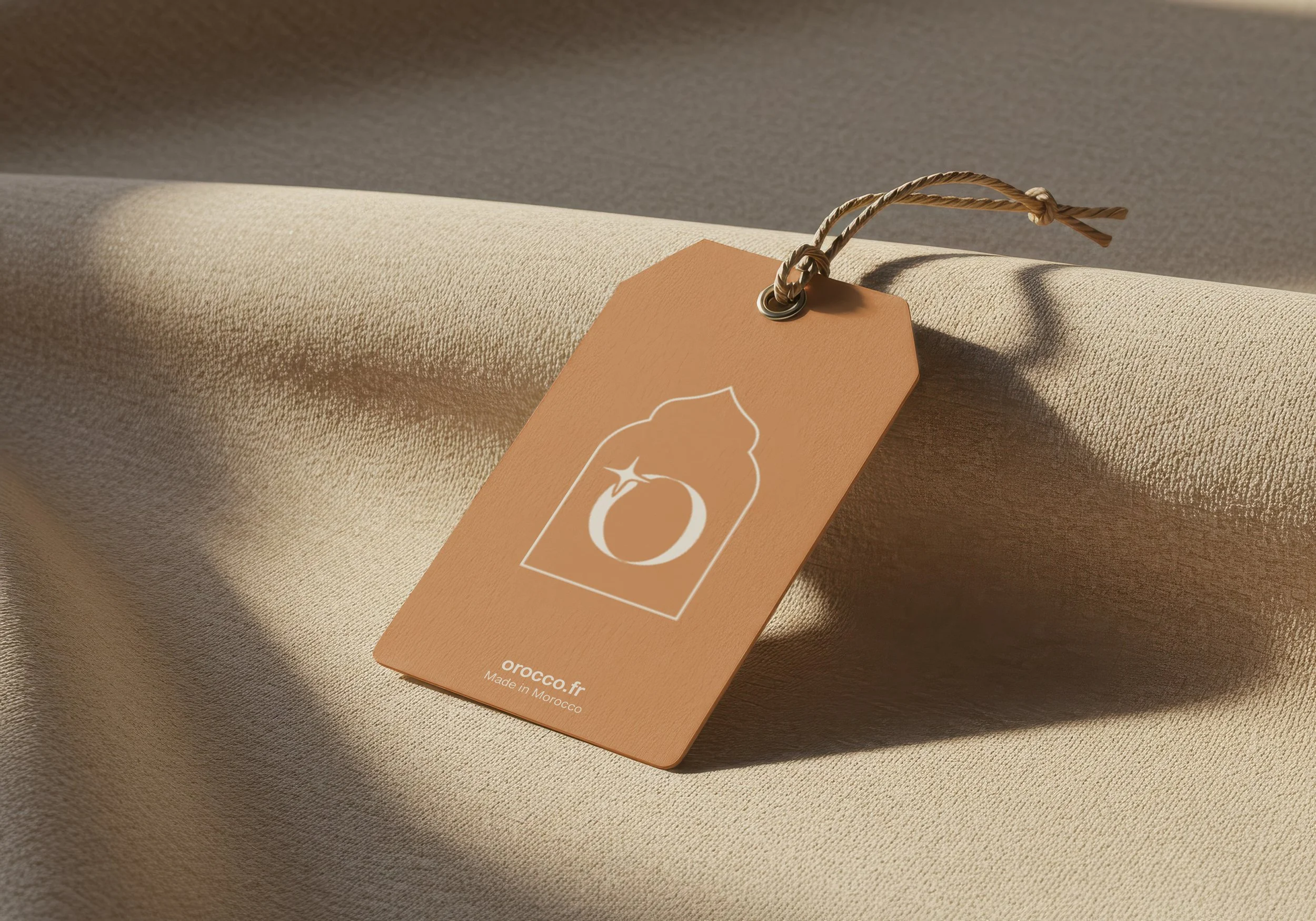 Étiquette en cuir beige avec un design de bague de fiançailles et la mention "orocco.fr" et "Made in Morocco" posée sur une surface en tissu beige avec une ombre douce.