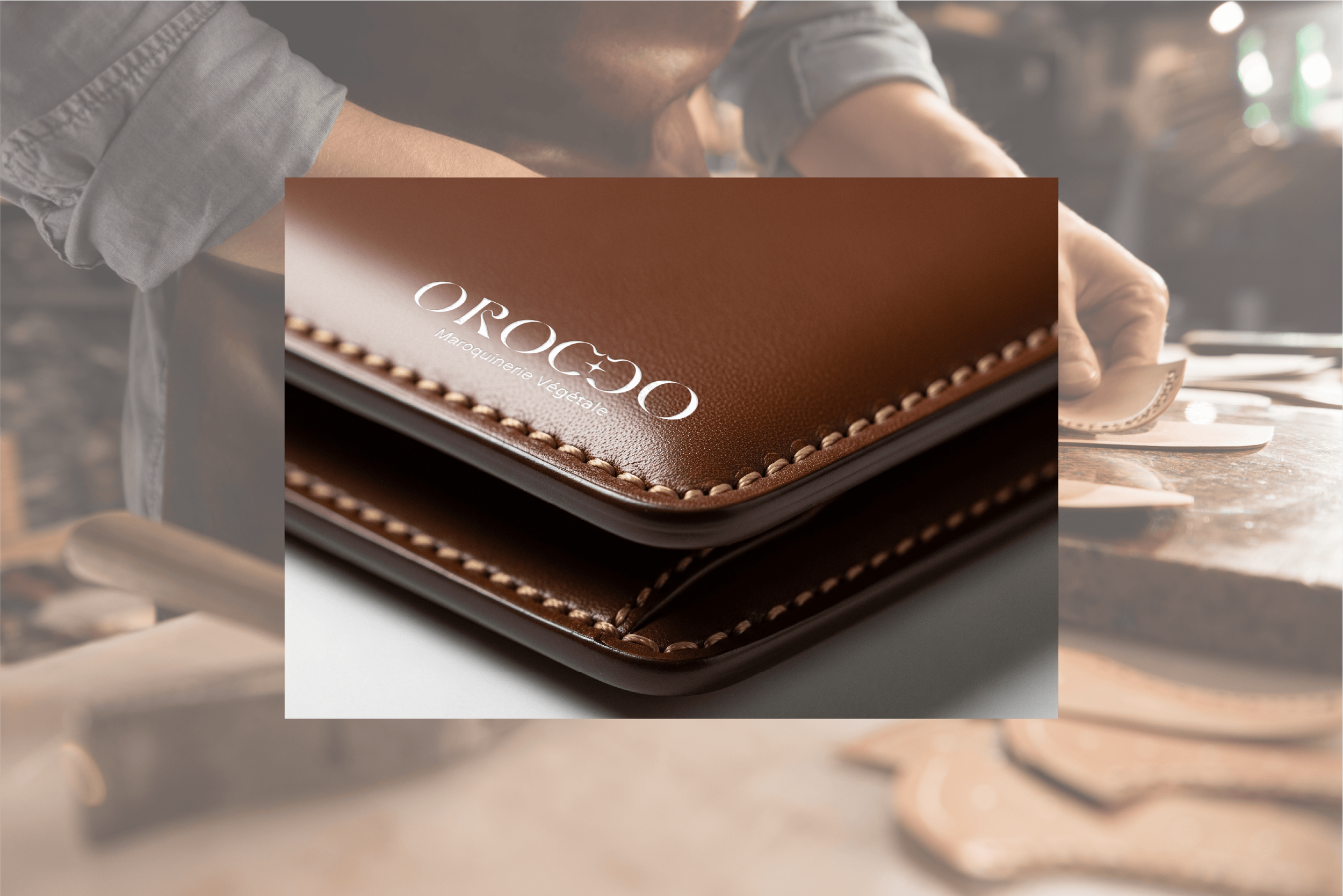 Prise de vue en gros plan d'un carnet en cuir marron avec le texte 'OROCÒ' et 'Marquinerie végétale' imprimés en blanc, avec une couture beige visible, posé sur un meuble en bois, dans un atelier de maroquinerie artisanale.