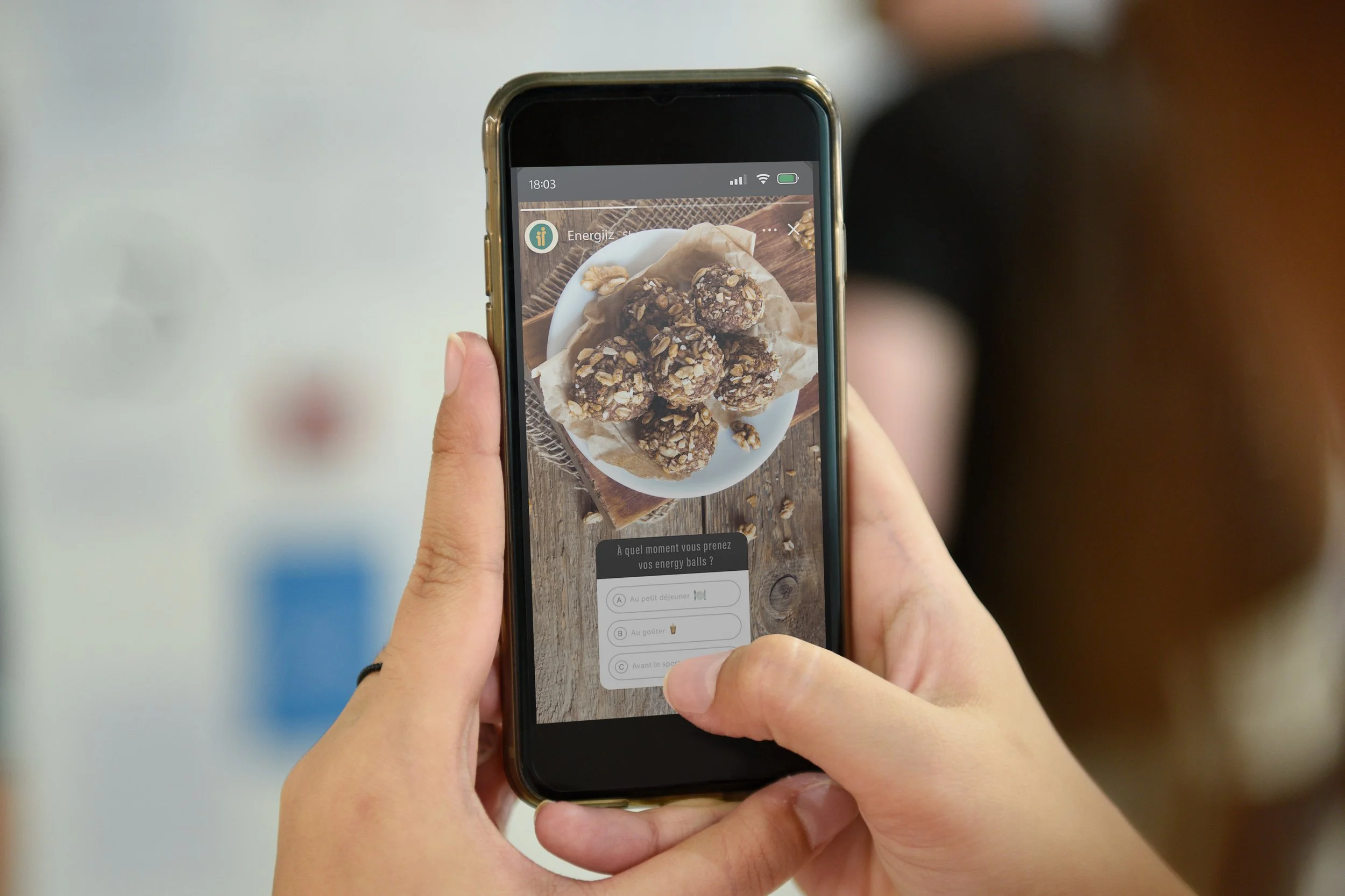Une personne tient un smartphone montrant une photo de boules d'énergie au chocolat et aux noix, avec un questionnaire en dessous.