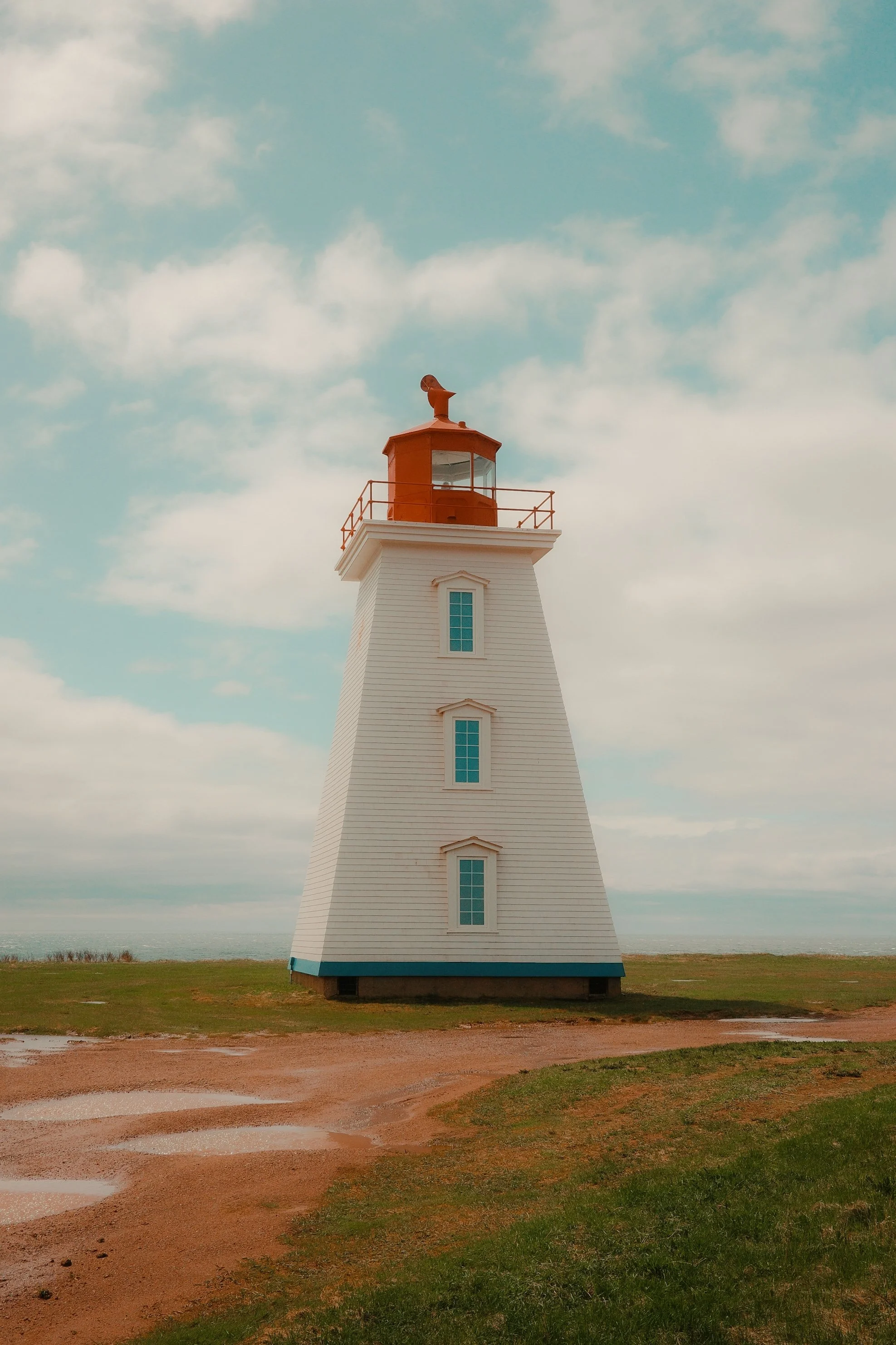 Un phare blanc avec une lanterne orange situé sur un terrain en plein air avec un ciel nuageux en arrière-plan.