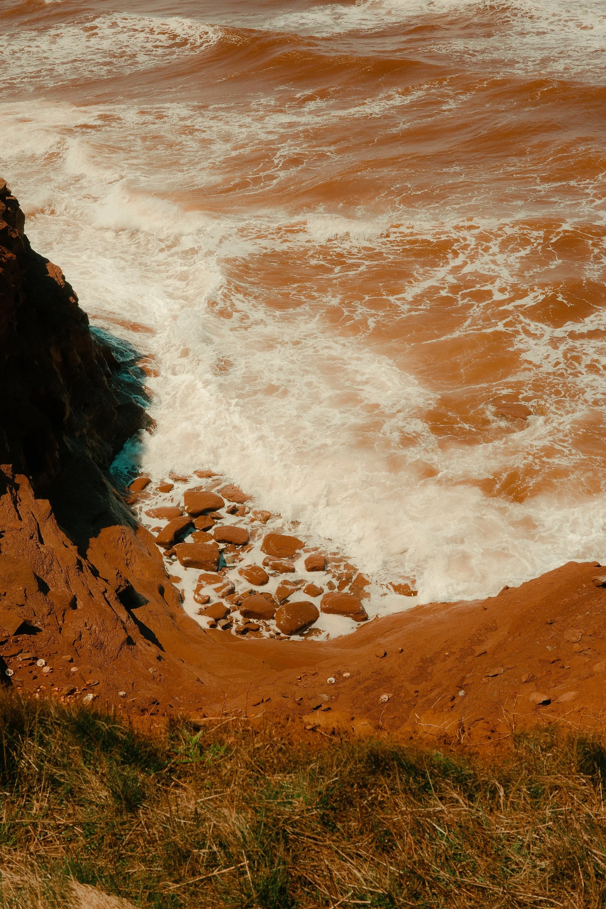 Côte rocheuse avec des vagues de mer agitées se brisant contre la falaise et des galets sur le rivage, sous un ciel nuageux, ambiance orageuse.