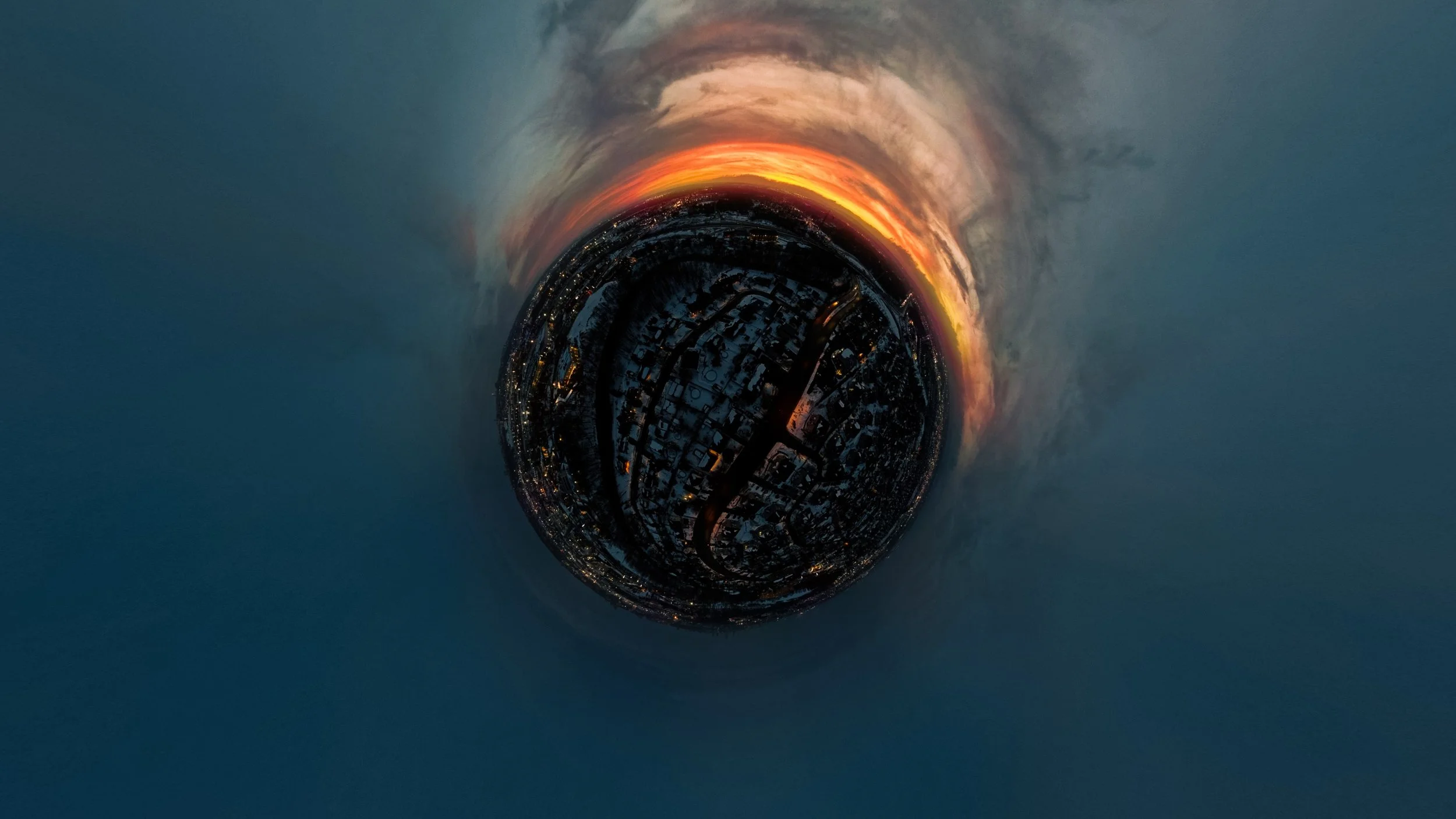 Vue aérienne d'une ville enneigée au crépuscule, avec le ciel orange et sombre, prises en mode 360 degrés, créant un effet de sphère.