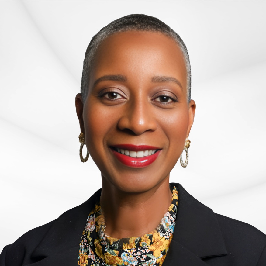A professional woman with short gray hair, wearing a black blazer, floral blouse, and gold hoop earrings, smiling against a white and gray background.