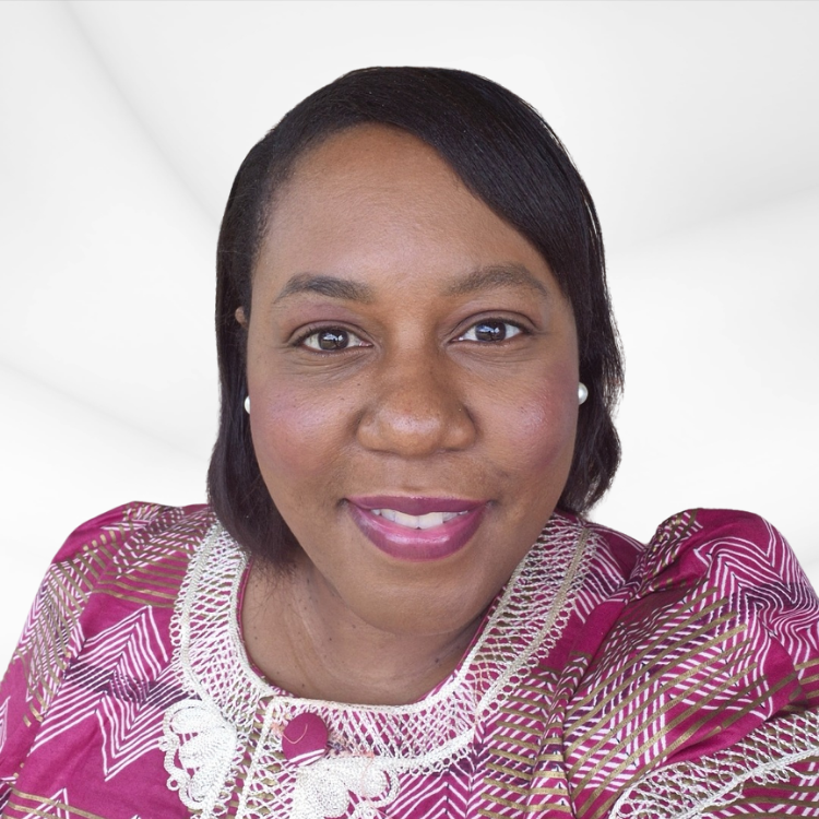 A woman with dark hair and dark eyes smiling, wearing a pink and gold patterned top with pearl earrings, against a white background.