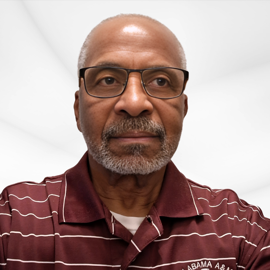 Close-up of an older man with glasses and a gray beard wearing a maroon and white striped polo shirt, standing in a bright, plain white room.