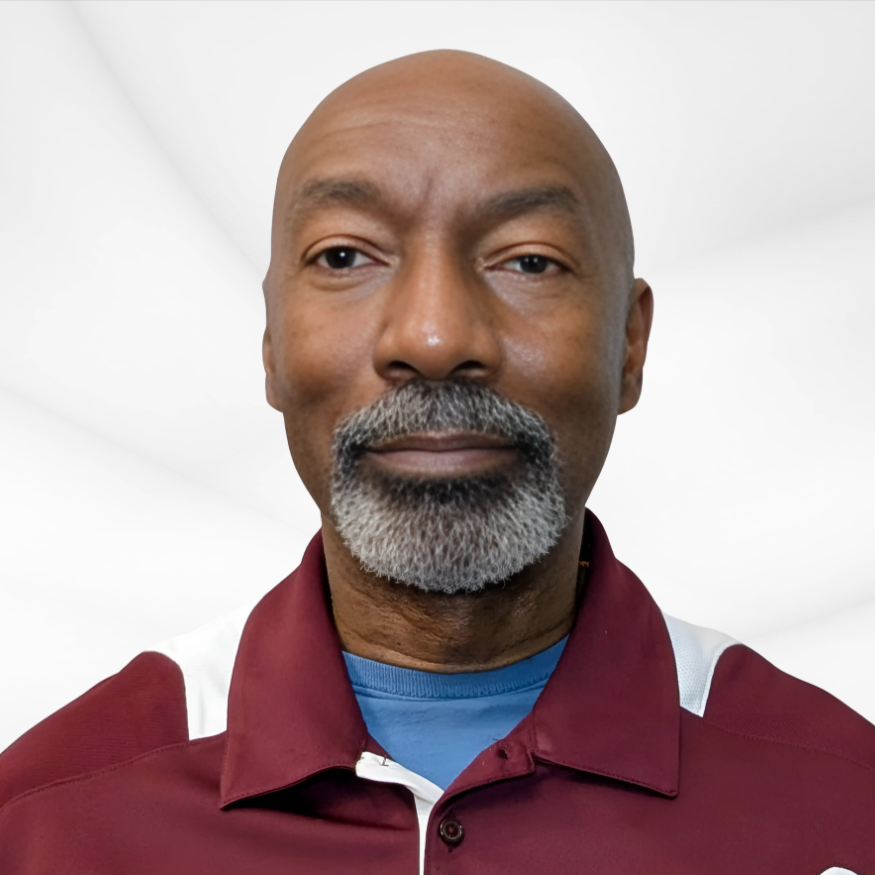 Close-up of a middle-aged man with a beard and mustache, wearing a maroon collared shirt, in a bright indoor setting.