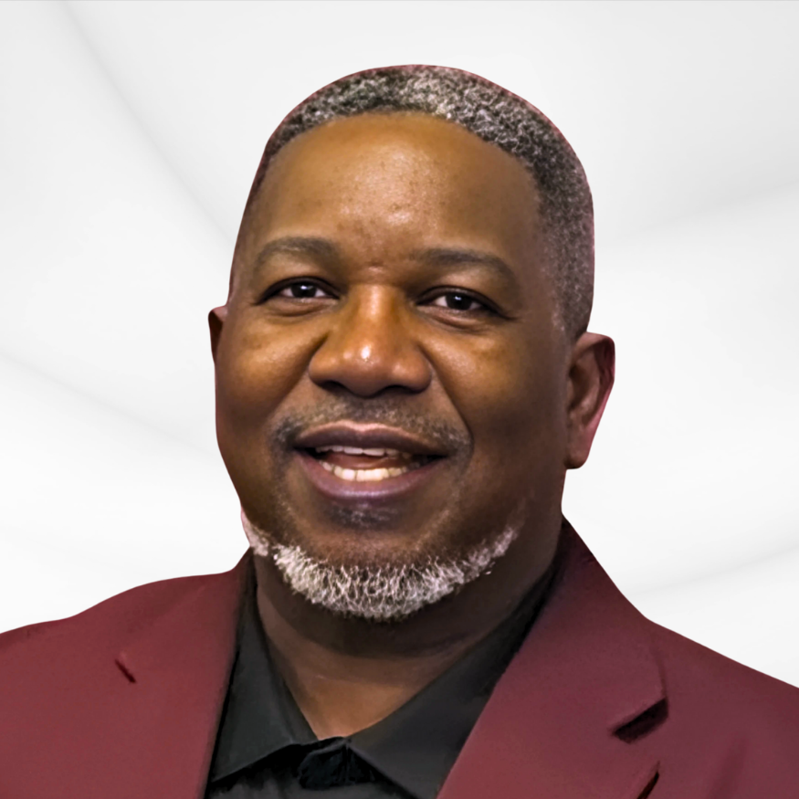 A headshot of a smiling man with short gray hair and a beard, wearing a burgundy blazer and black shirt, against a plain white background.