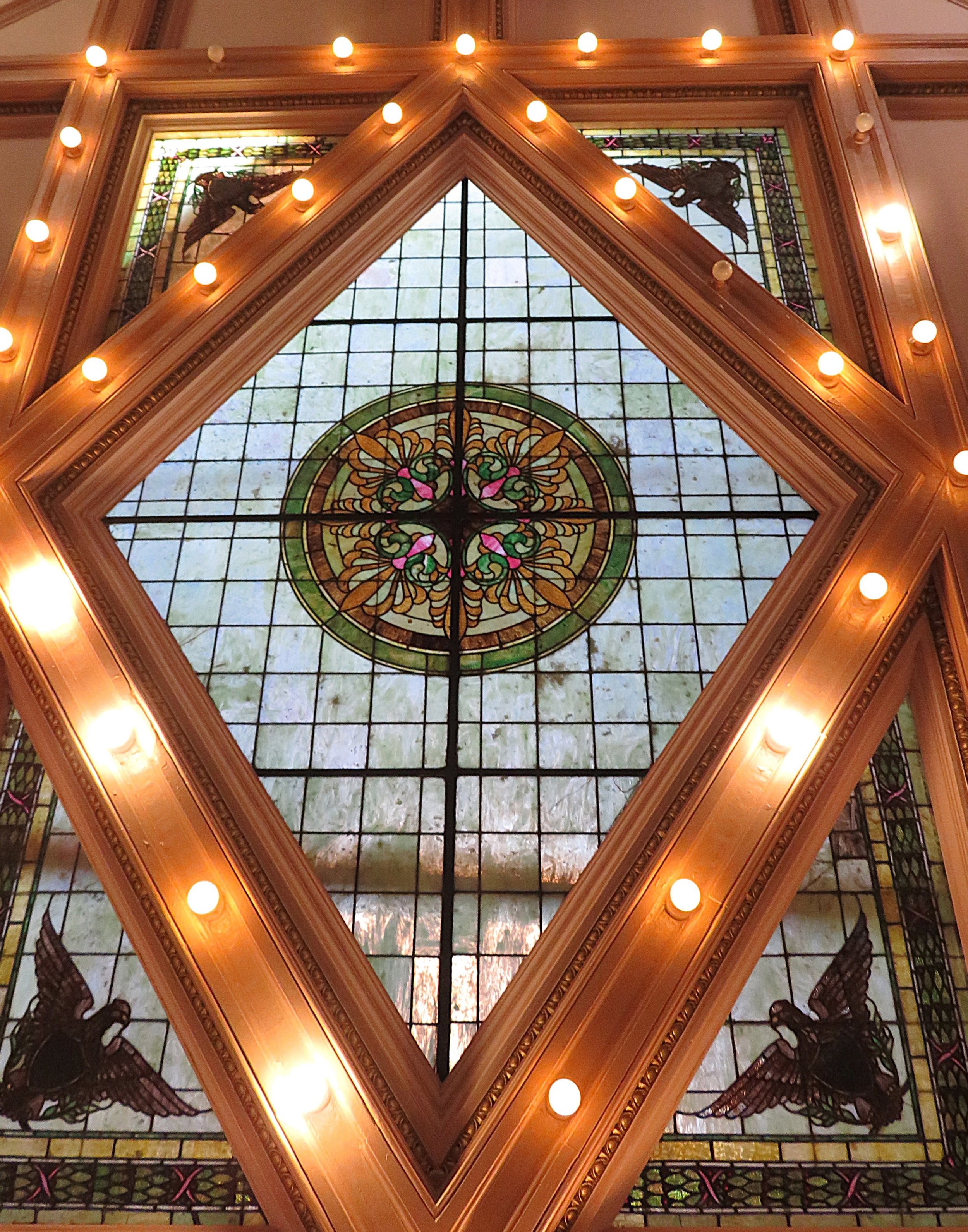Decorative stained glass ceiling with illuminated border lights, featuring floral design and black angel motifs.