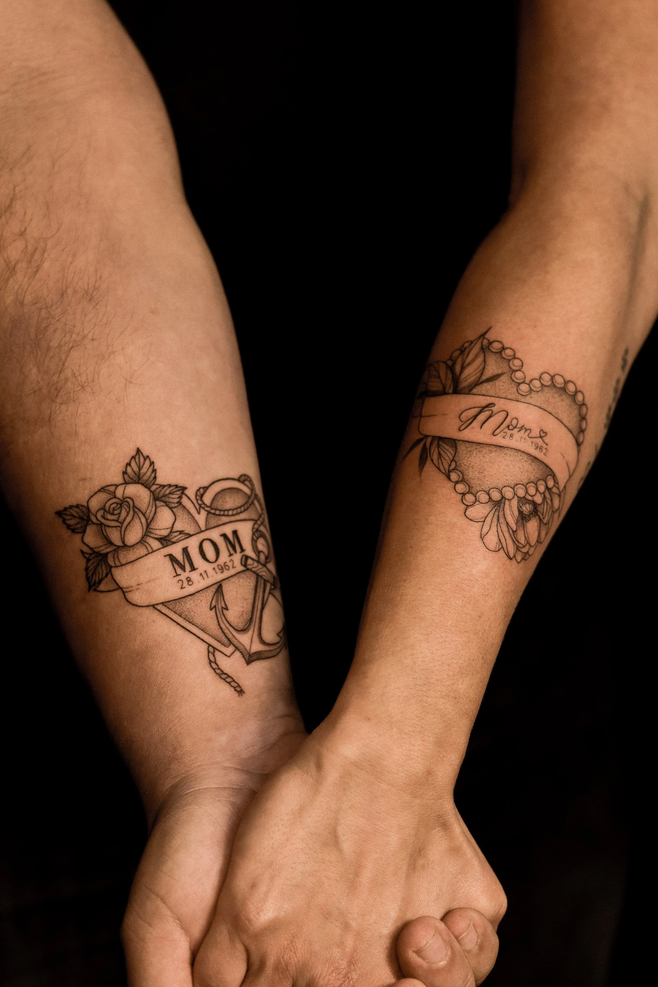 Tatoeages van een hart met een roos, anker en een band met de tekst 'Mom' en een datum.