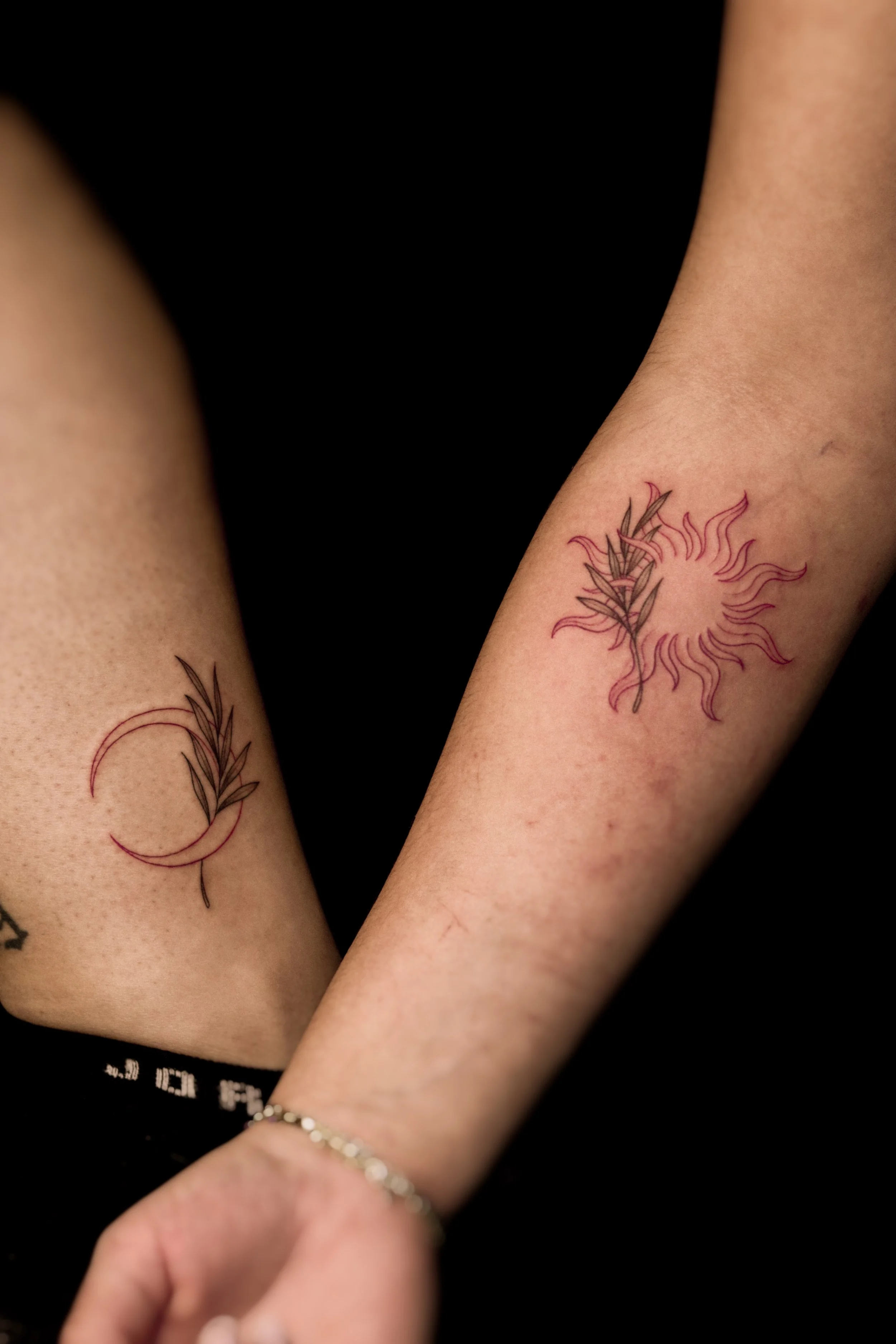 Tatoeages van een blad met planten en een zon in roze en zwart op de onderarm van twee personen