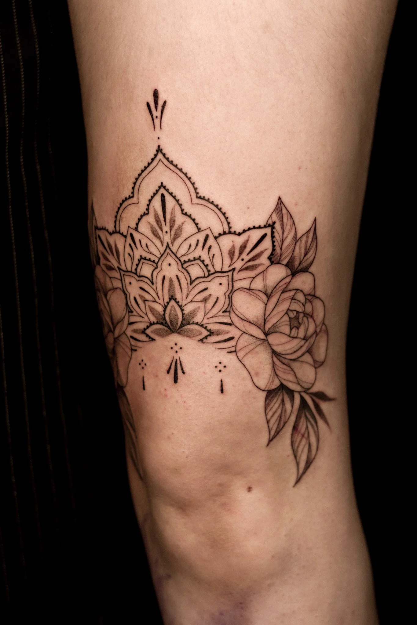 Tattoo van een mandala met bloemen en bladeren op een arm.