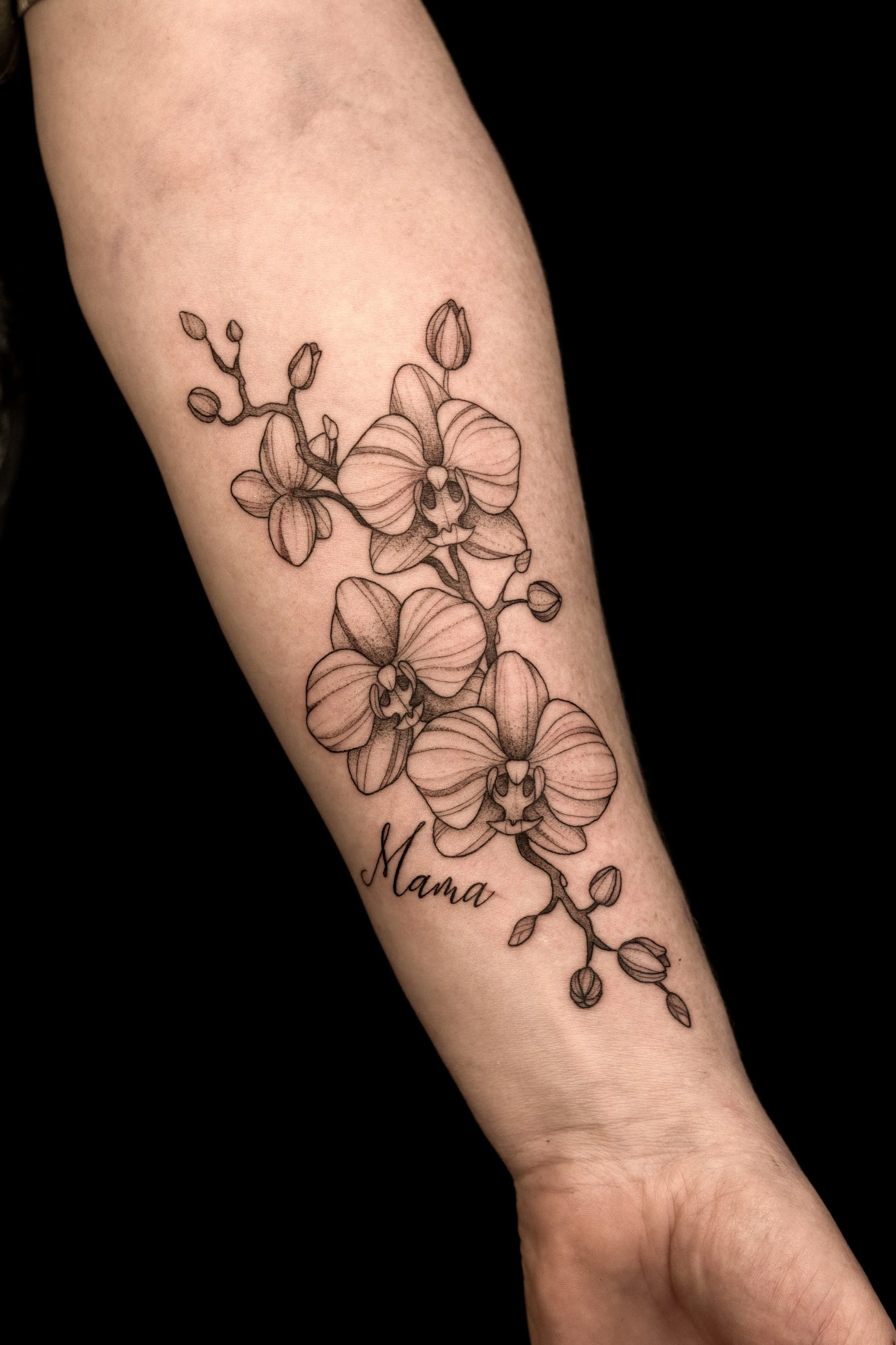 Tattoo van een orchidee met de naam 'Mama' op de onderarm.