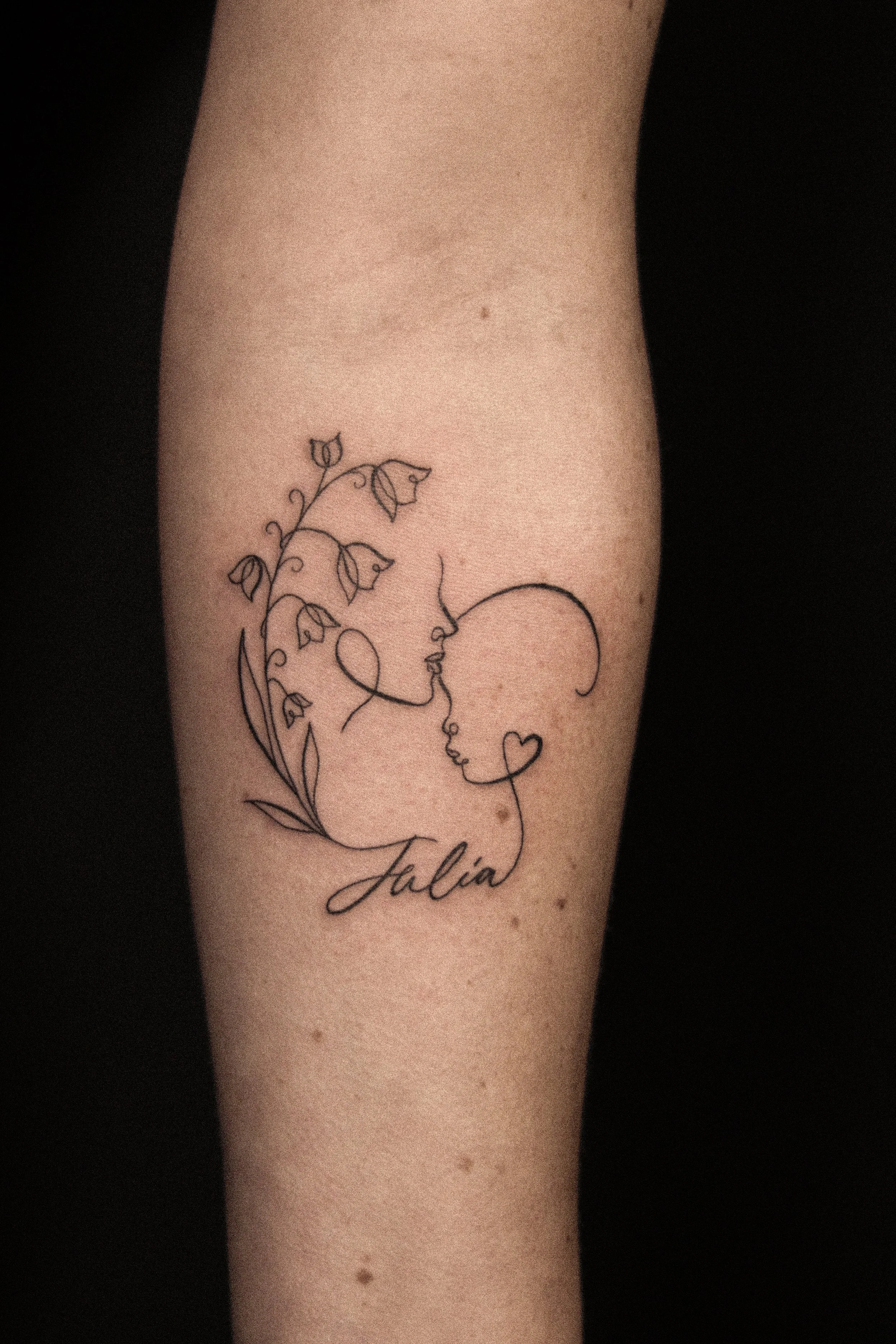 Tatoeage van een vrouw en een babyhoofd, met bloemen en de naam 'Julia'.