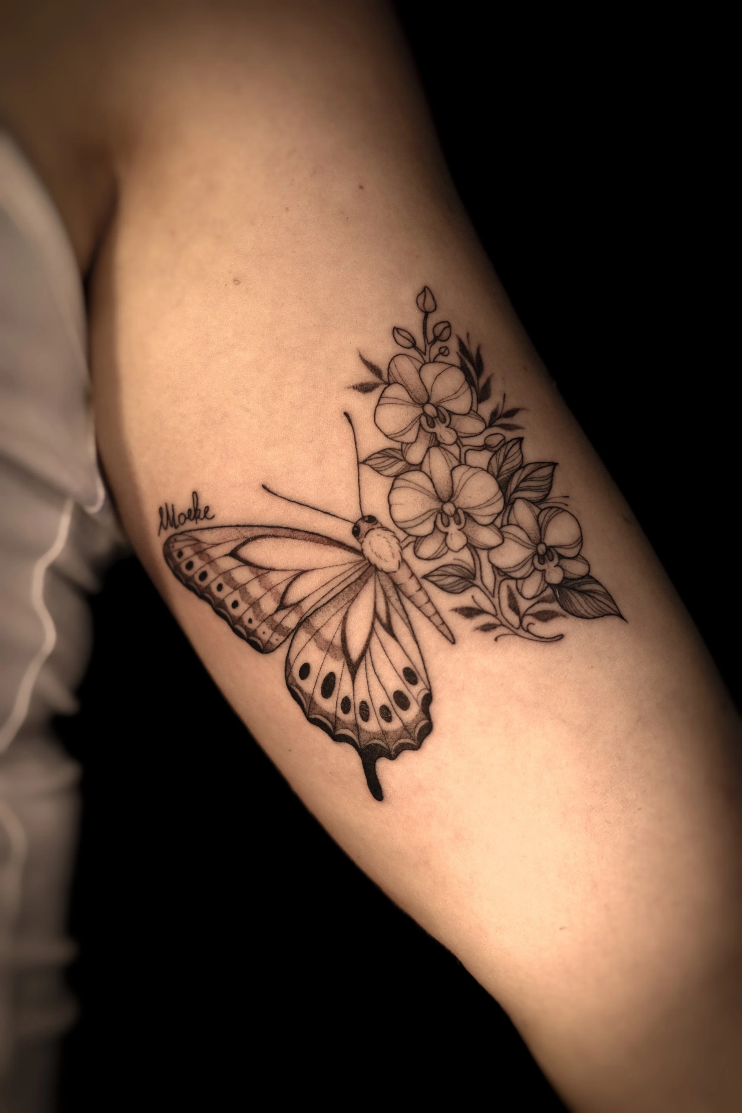 Tatoeage van een vlinder met bloemen en bladeren op de bovenarm.