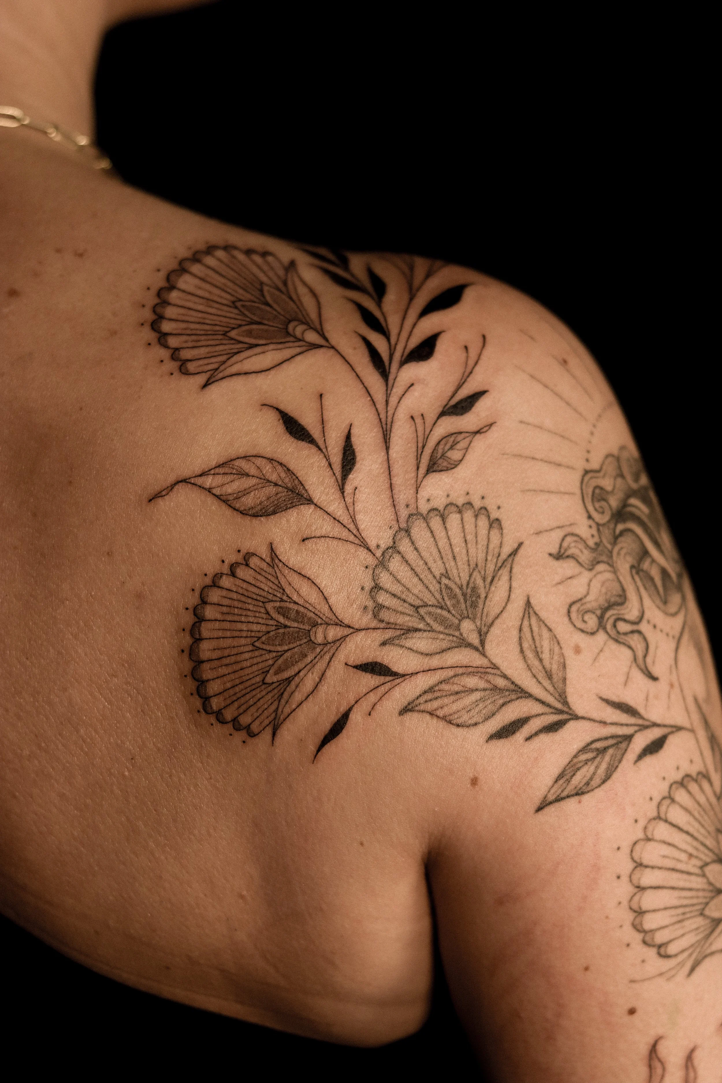 Tatoeage van bloemen en bladeren op schouder en borst.